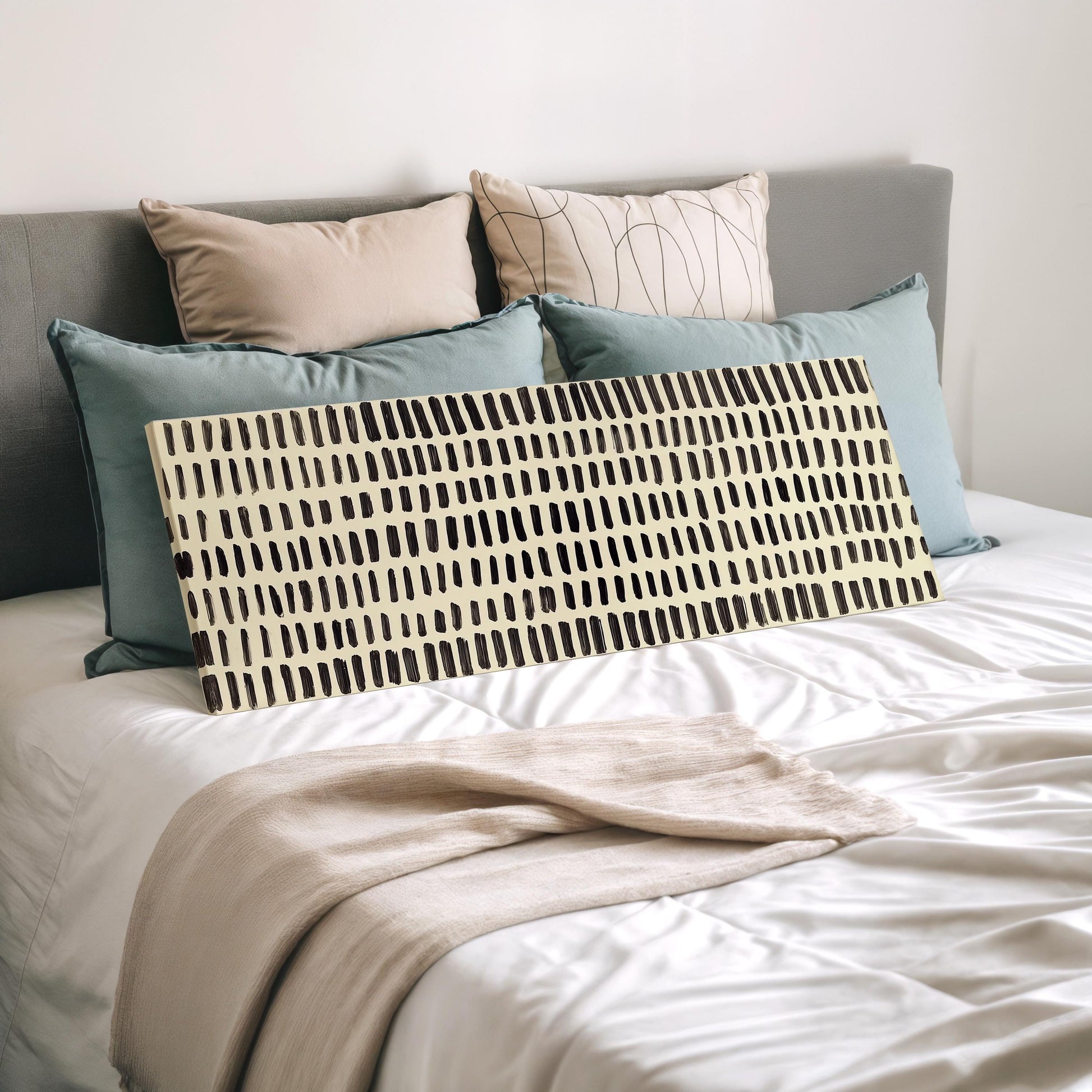 a neatly made bed with a white comforter and a large, patterned throw blanket. The bed is adorned with several pillows, including a gray pillow, a beige pillow, and a black and white striped pillow. The pillows are arranged in a visually appealing manner, creating a cozy and inviting atmosphere.