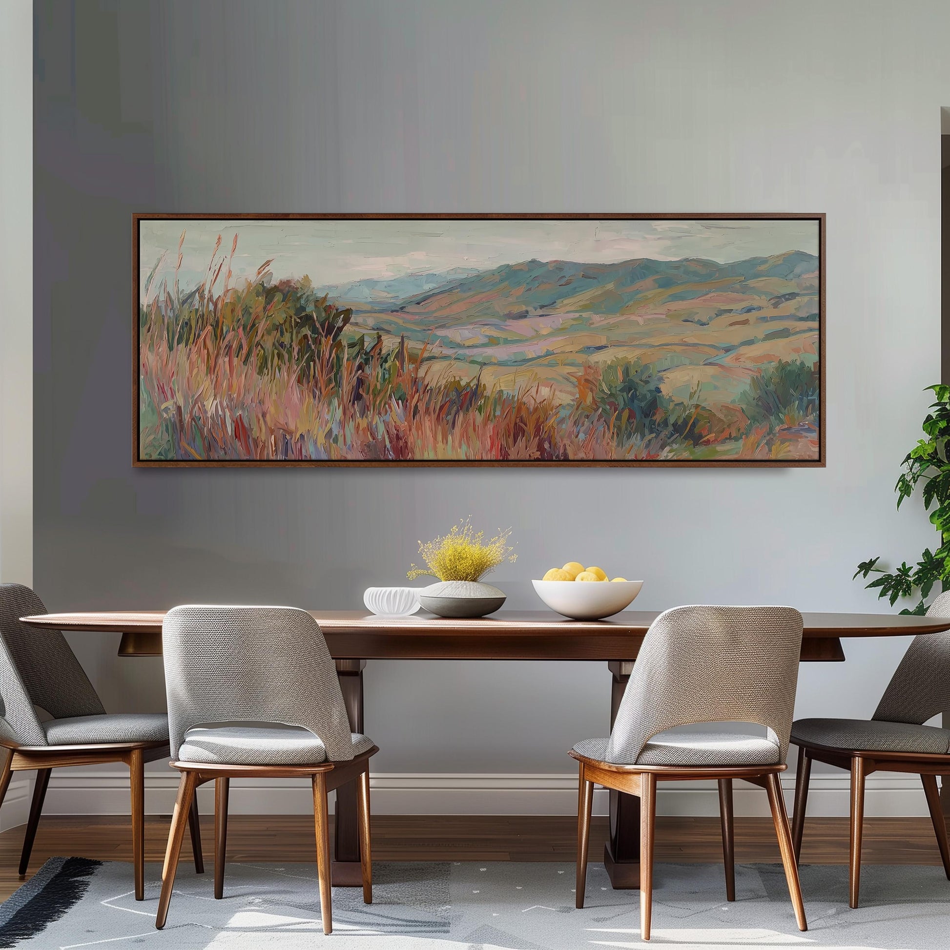 a dining room with a large painting of a countryside landscape hanging on the wall above a wooden dining table with four chairs. The table is set with a bowl of fruit and a vase of flowers, creating a cozy and inviting atmosphere.