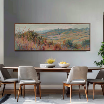 a dining room with a large painting of a countryside landscape hanging on the wall above a wooden dining table with four chairs. The table is set with a bowl of fruit and a vase of flowers, creating a cozy and inviting atmosphere.