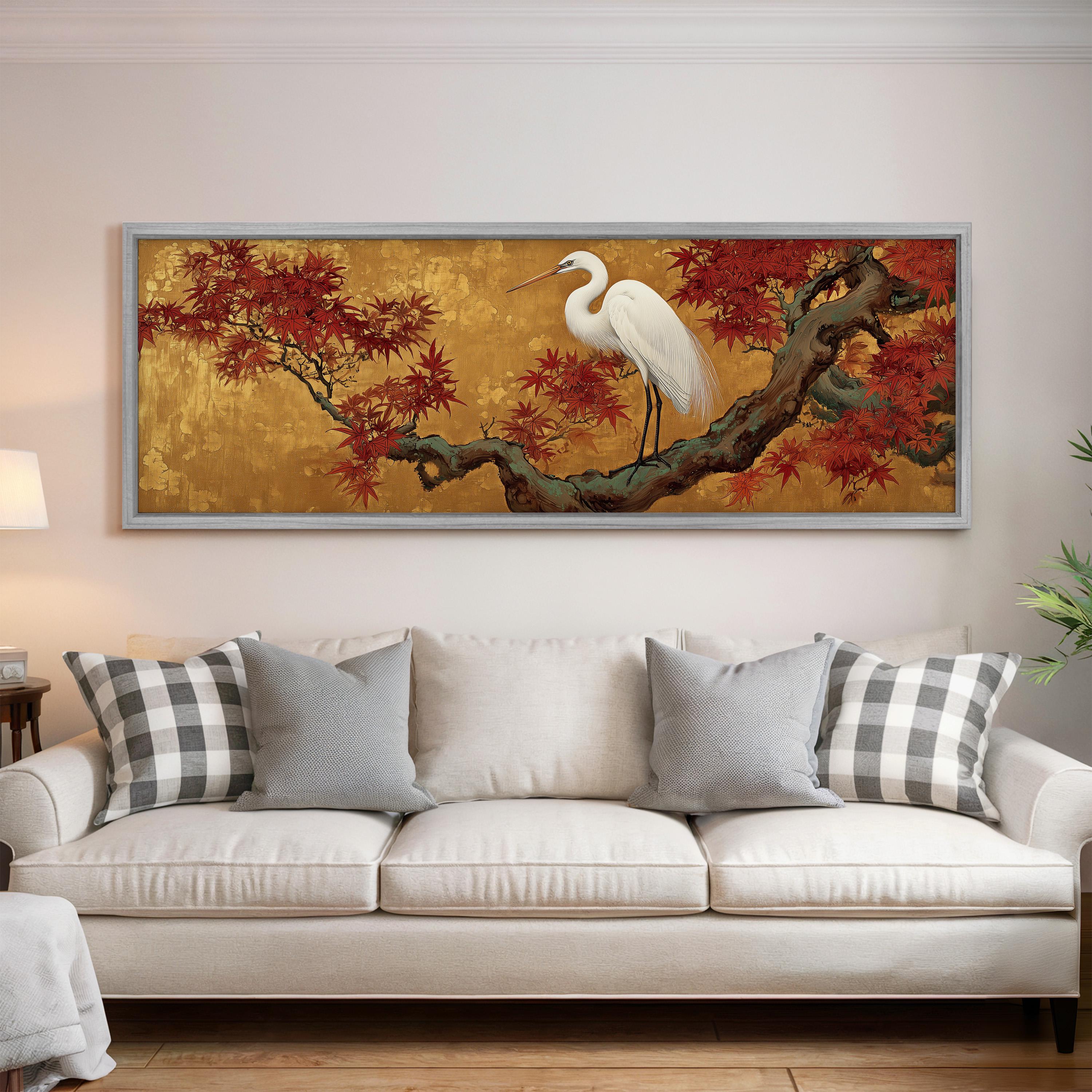 a large, framed painting of a white heron perched on a branch with red leaves, hanging on a wall above a white couch with gray and white plaid throw pillows.