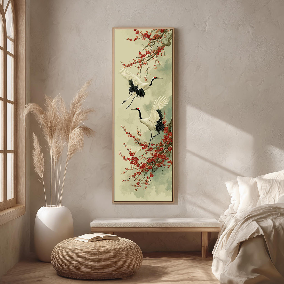 a serene and minimalist bedroom setting with a large framed painting of two cranes in flight hanging on the wall. The painting is surrounded by a white vase filled with tall, light-colored reeds, and a woven ottoman is placed in front of the painting. The room has a clean, uncluttered appearance with a bed and a window providing natural light.