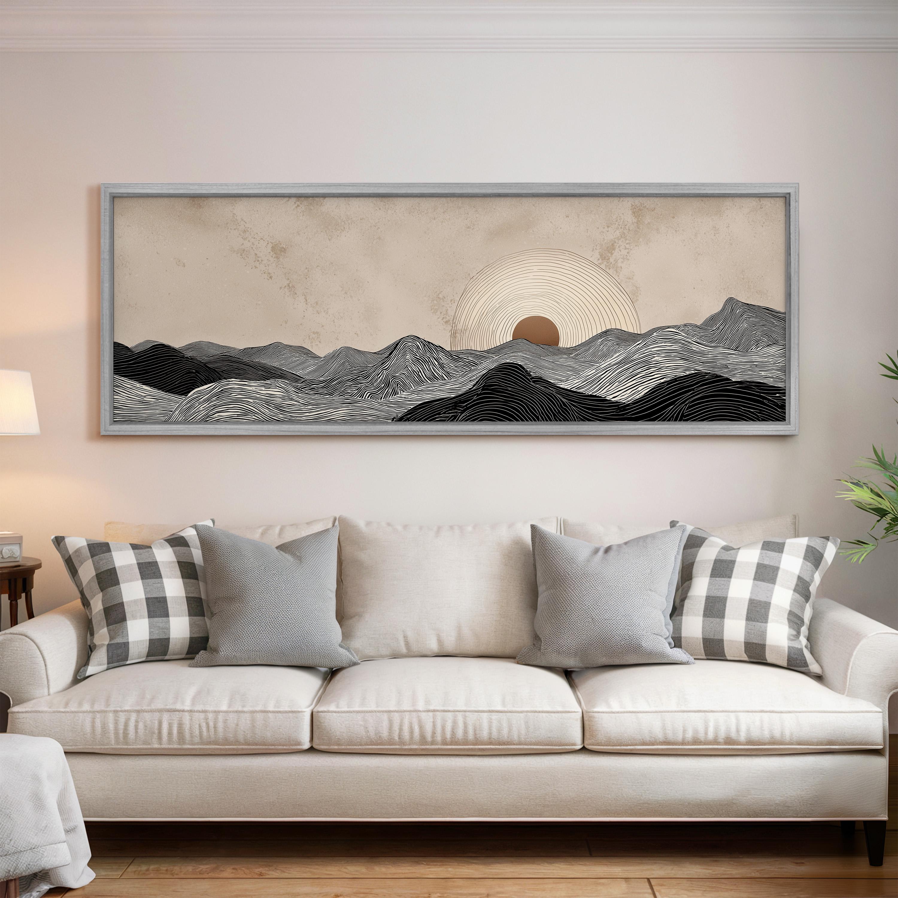 a large, framed artwork depicting a serene landscape with mountains and a sun in the sky, hanging above a white couch with patterned throw pillows.