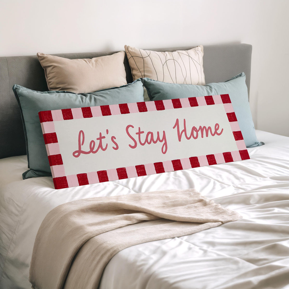 Let's stay home sign with a red checked border wide panoramic canvas print laid on a bed to show its size