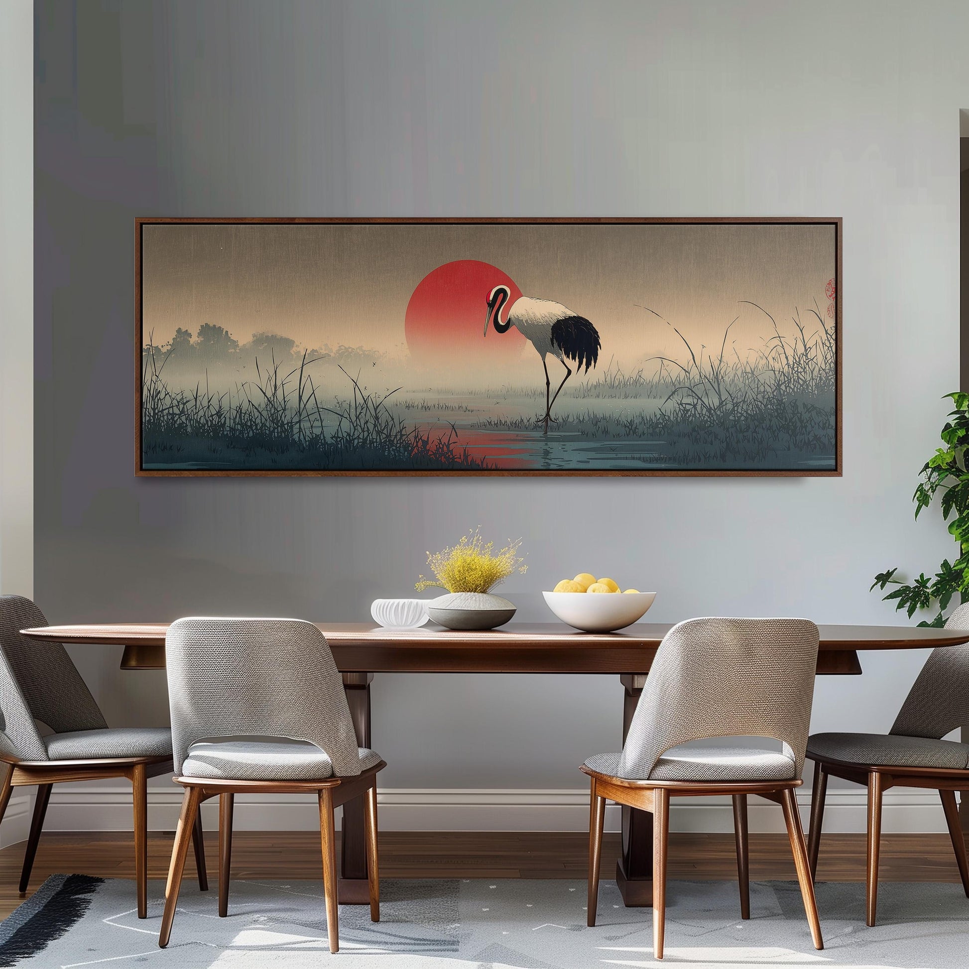 a large painting of a crane standing in a field with a red sun in the background, hanging on a wall above a wooden dining table with four chairs.