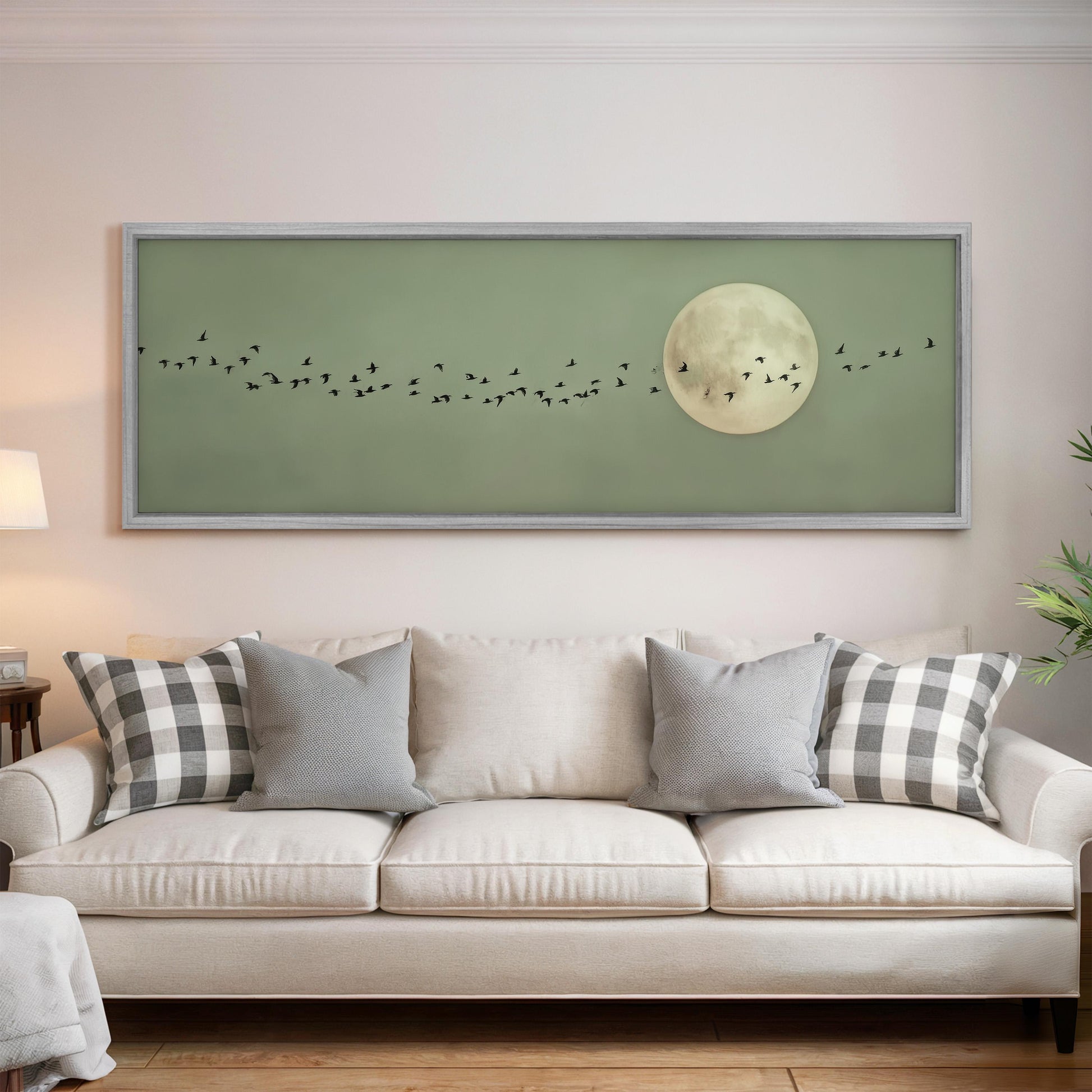 a large framed artwork depicting a flock of birds flying in front of a full moon on a green background.