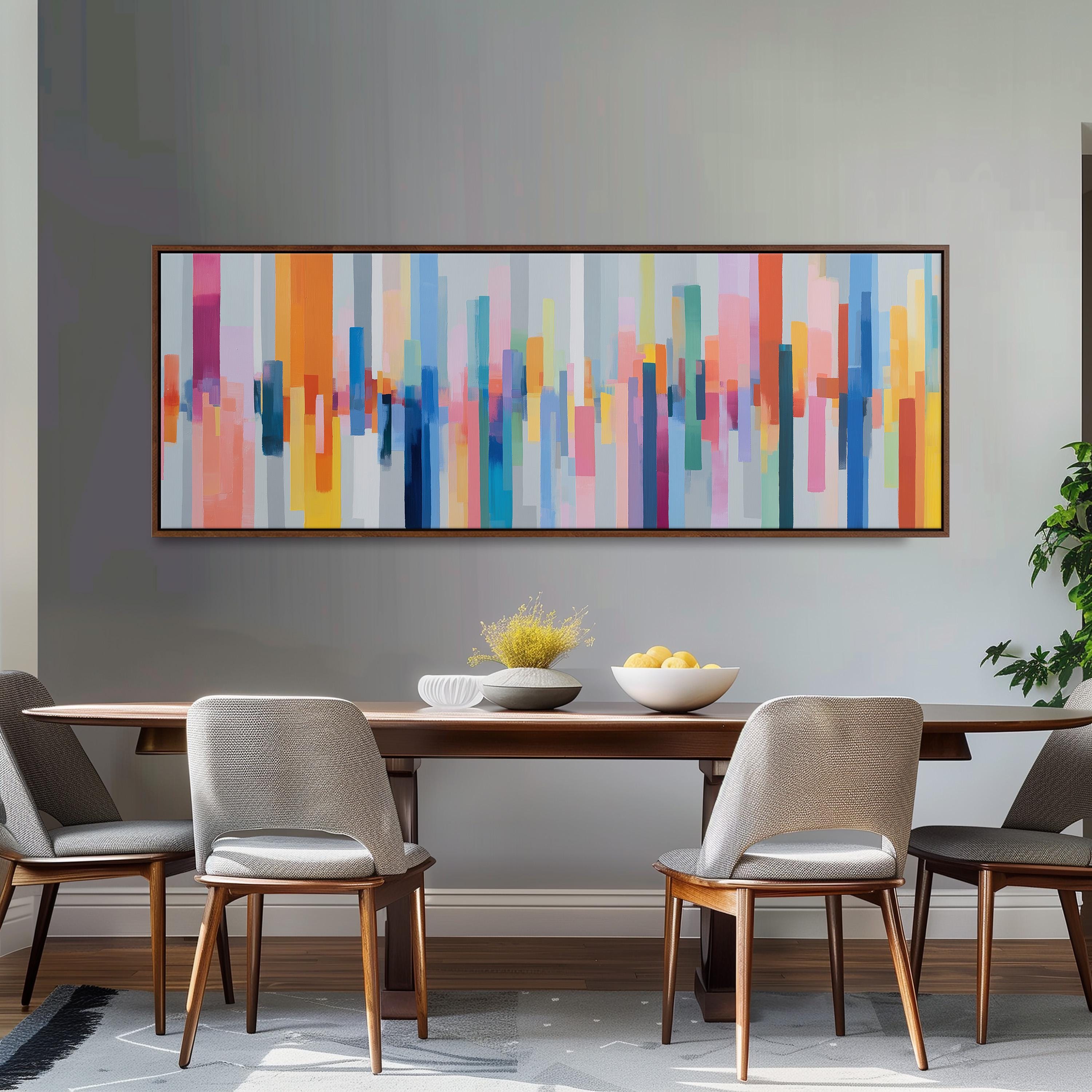 a modern dining room with a wooden table and four chairs. Above the table, there is a large abstract painting with vertical stripes in various colors, including shades of orange, pink, blue, and yellow. The painting is framed and hangs on the wall above the table.
