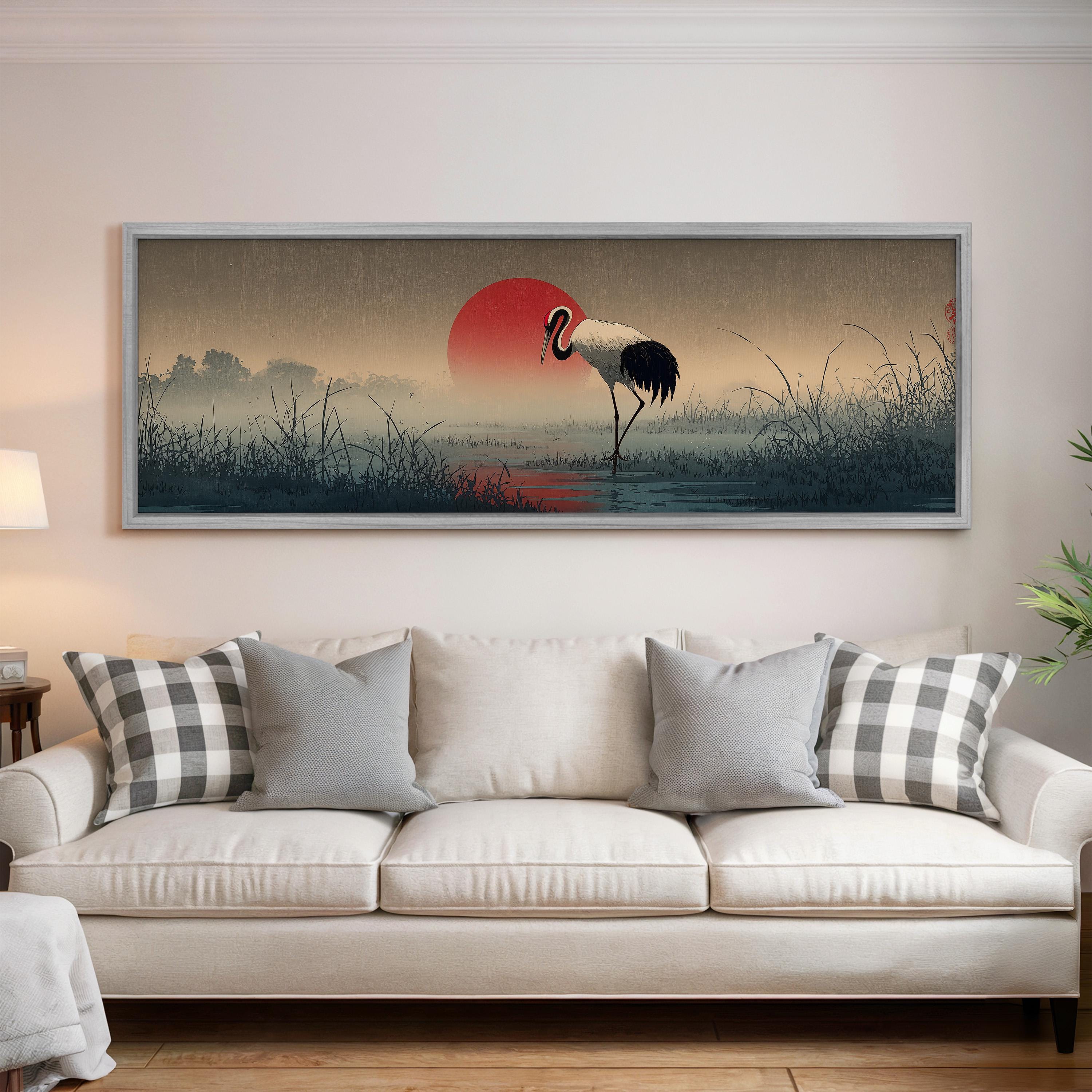a large framed painting of a crane standing in a field with a red sun in the background.