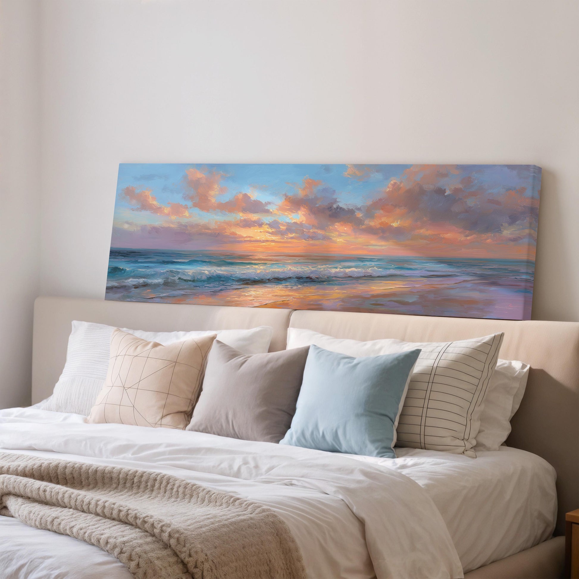 a large painting of a sunset over the ocean, hanging above a bed with white pillows and a gray blanket.