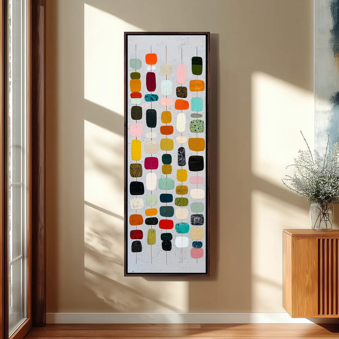 a large abstract painting hanging on a wall, with a wooden cabinet and a vase of flowers to the right of the painting.