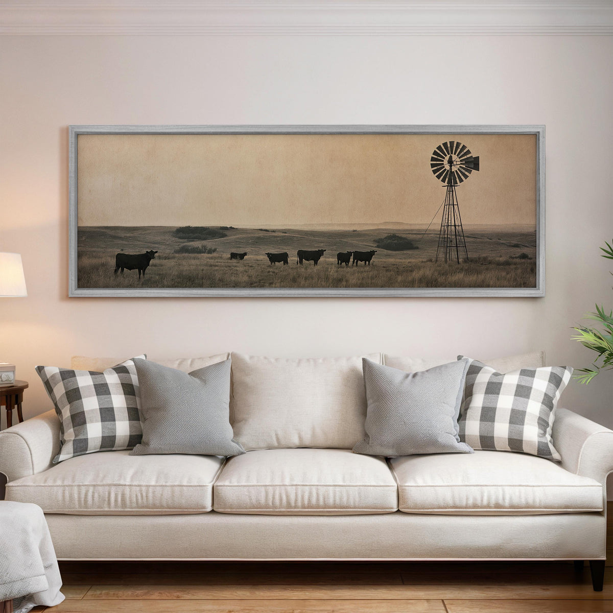 Black cattle grazing by a windmill on the prairie panoramic canvas print above a white sofa in a bright living room