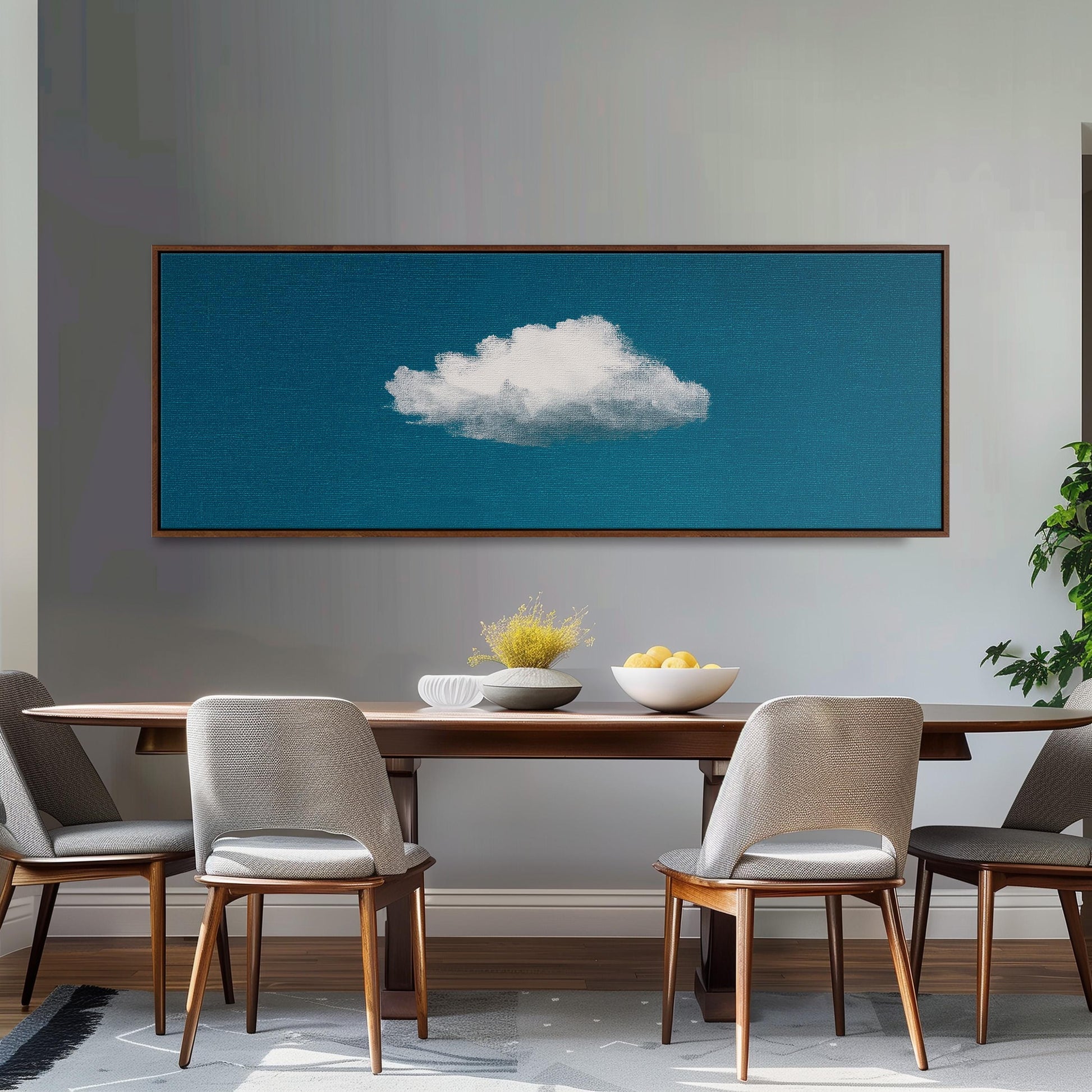 a dining room with a wooden table and four chairs, a large framed artwork of a cloud on the wall above the table, and a bowl of fruit on the table.