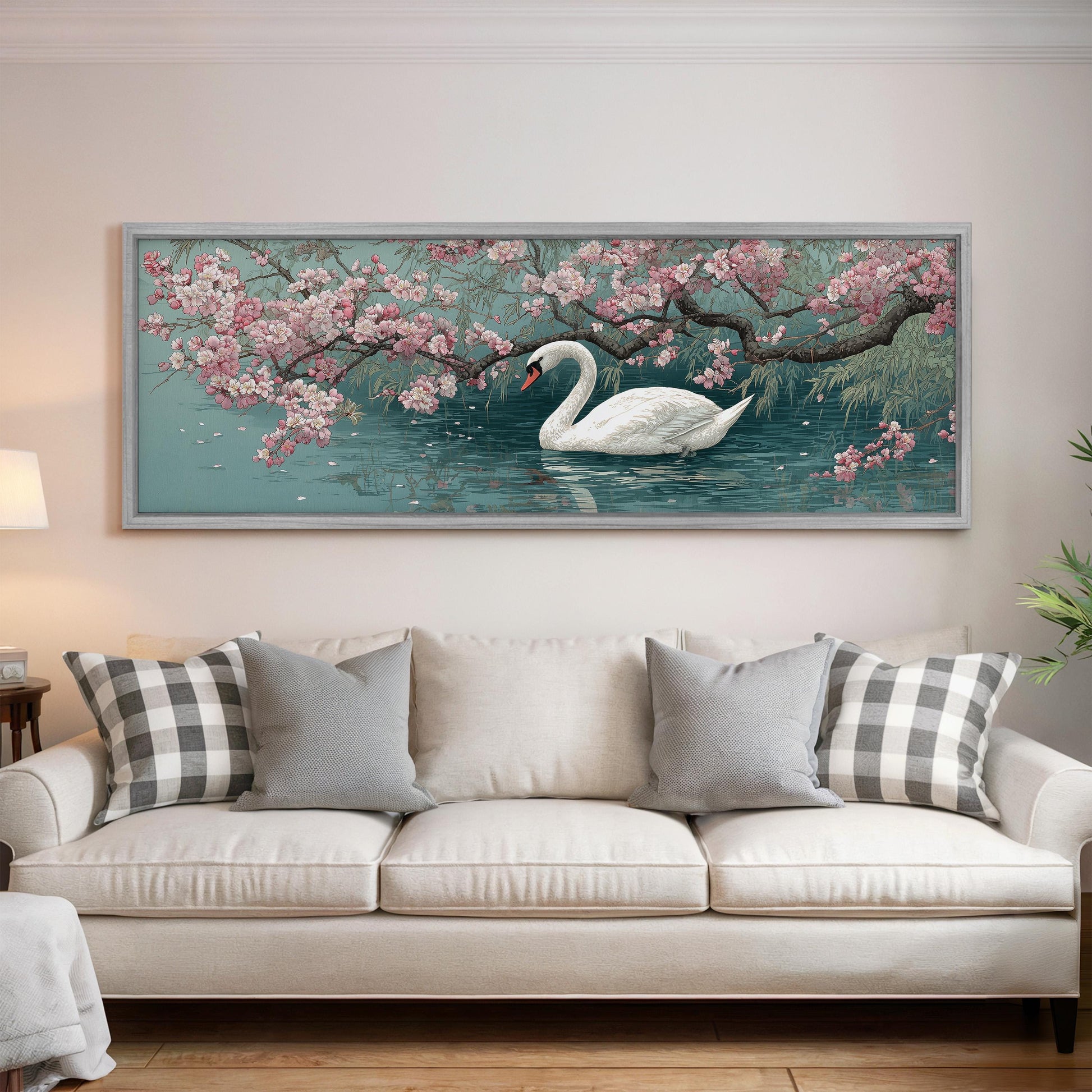 A large framed painting of a swan swimming in a pond with pink flowers is hanging on the wall above a white sofa with gray and white patterned pillows.