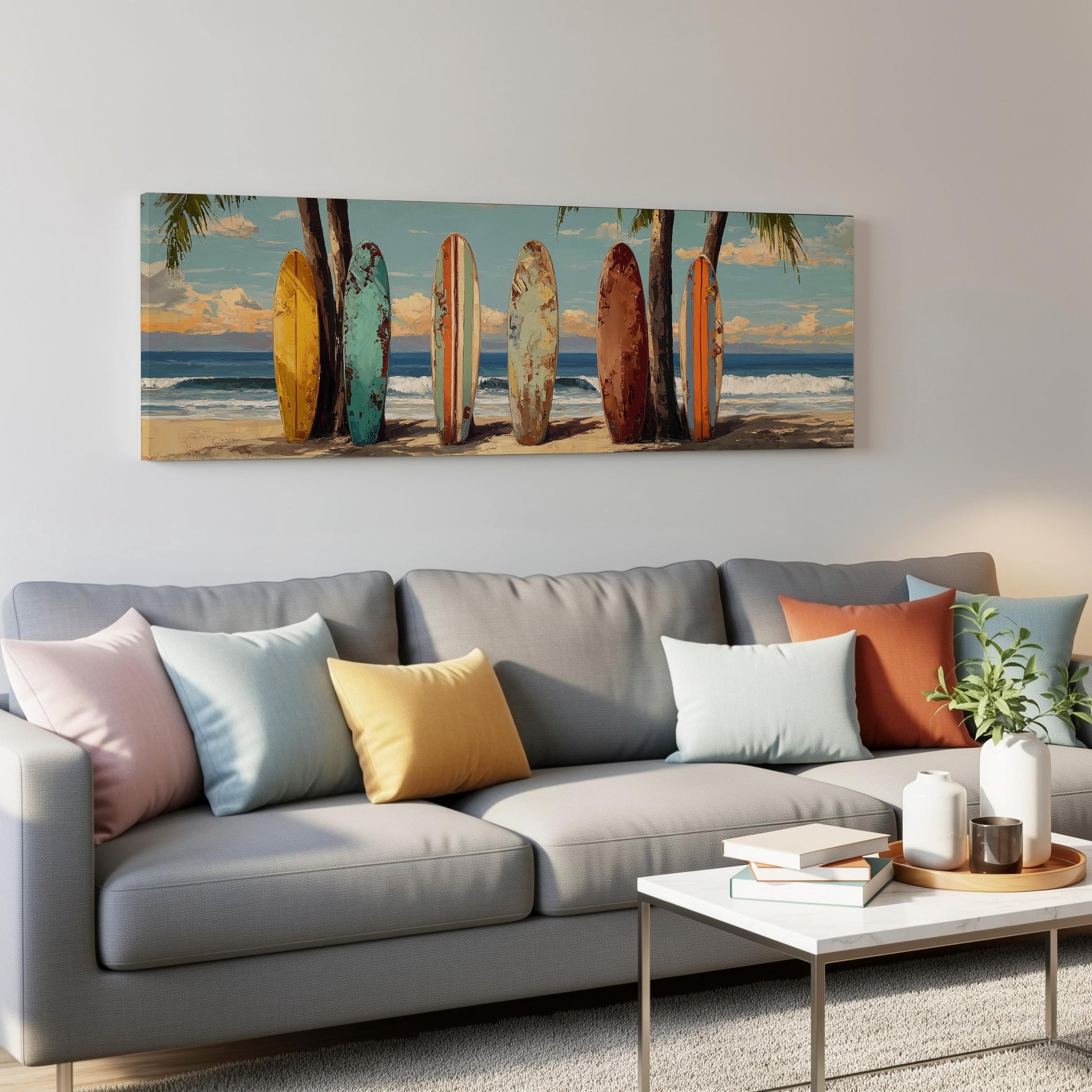 a living room with a gray sofa adorned with colorful throw pillows. Above the sofa, there is a large painting depicting a beach scene with surfboards lined up on the sand.