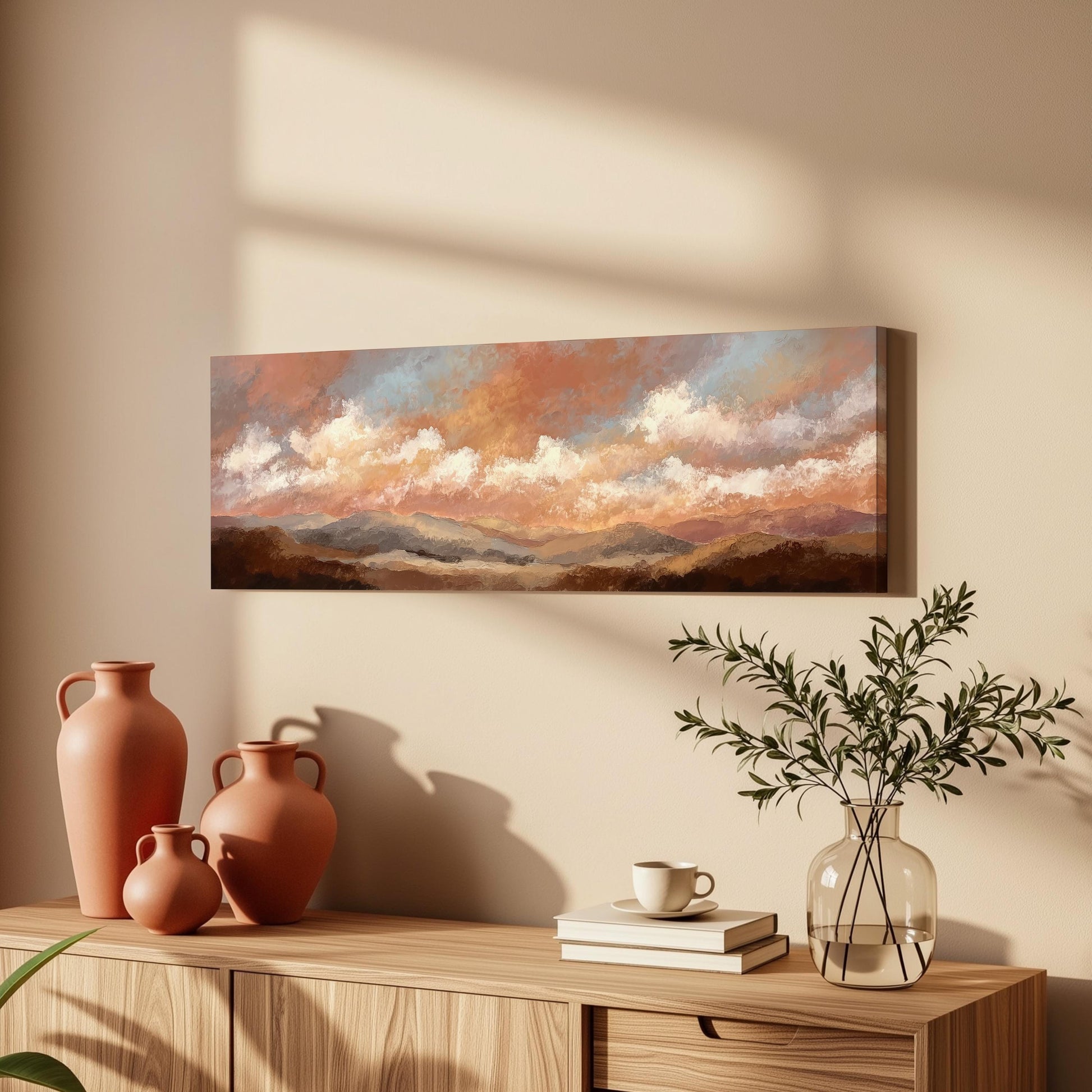 a wooden cabinet with a painting of a landscape hanging on the wall above it. The cabinet also has three orange vases and a glass vase with greenery, as well as a stack of books and a coffee cup on the surface.