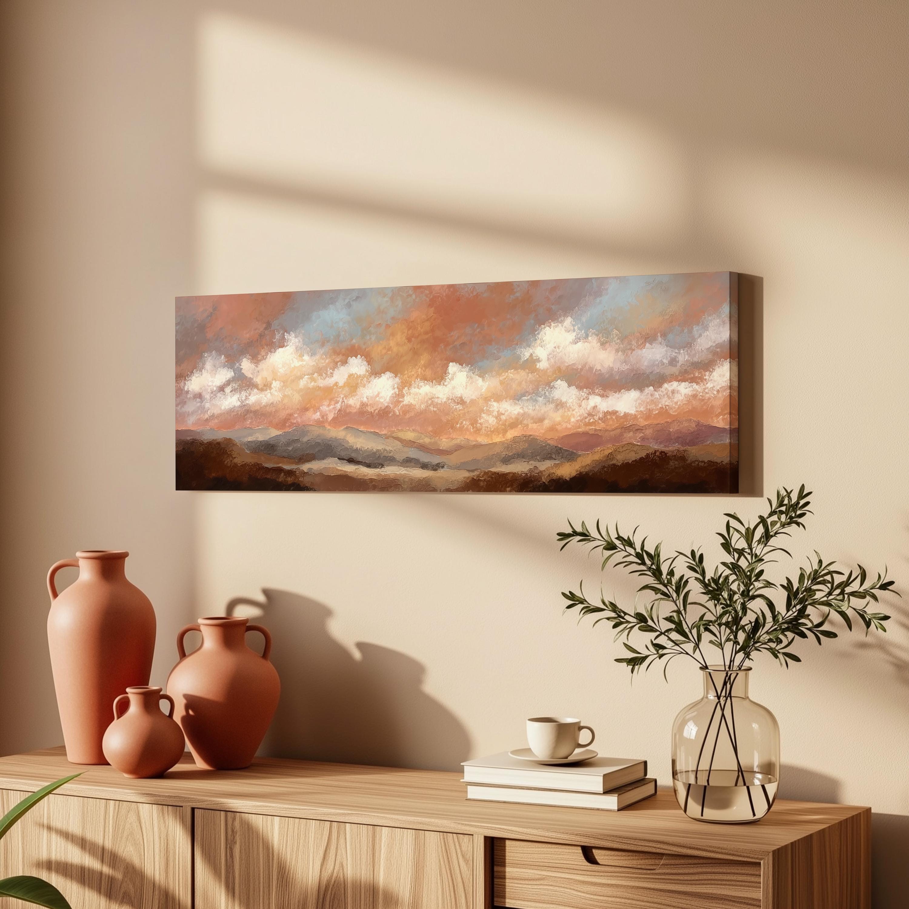 a wooden cabinet with a painting of a landscape hanging on the wall above it. The cabinet also has three orange vases and a glass vase with greenery, as well as a stack of books and a coffee cup on the surface.