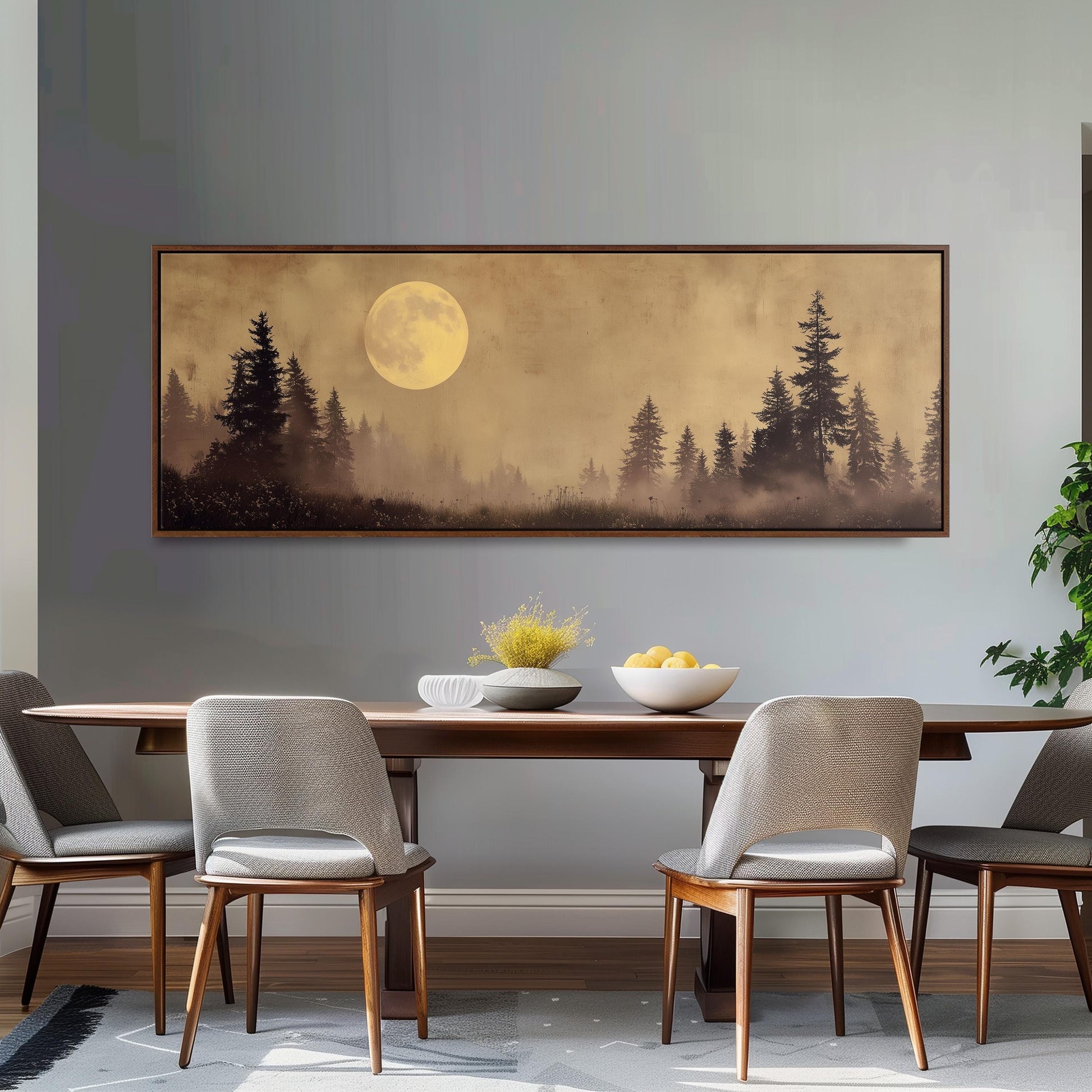 a dining room with a large framed landscape painting hanging on the wall above a wooden dining table. The painting depicts a serene forest scene with a full moon in the background. The table is set with a bowl of fruit and a vase of flowers, creating a cozy and inviting atmosphere.