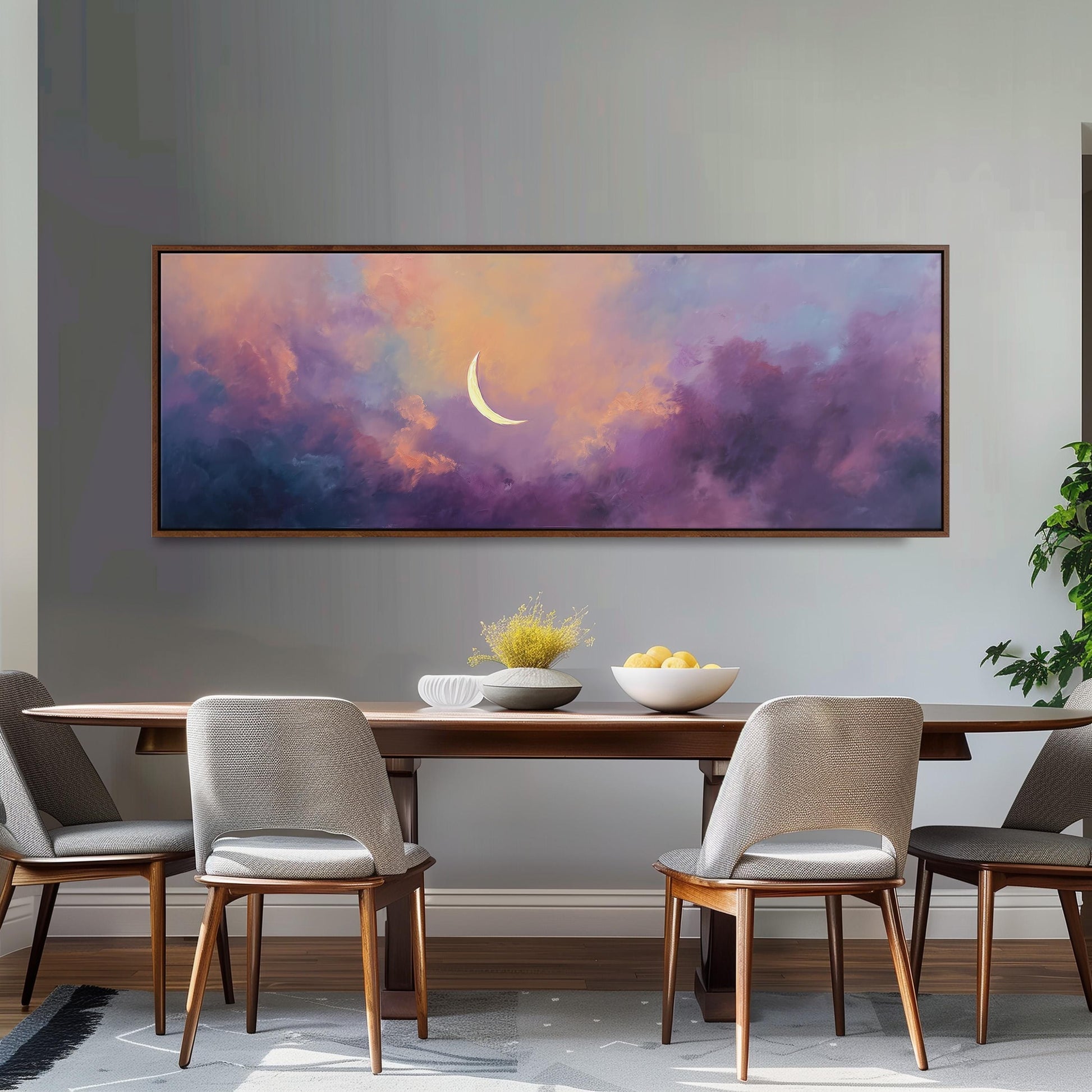 a dining room with a large painting of a crescent moon and a colorful sky above a wooden table with four chairs. The painting is hanging on the wall above the table, which is set with a bowl of fruit and a vase of flowers.