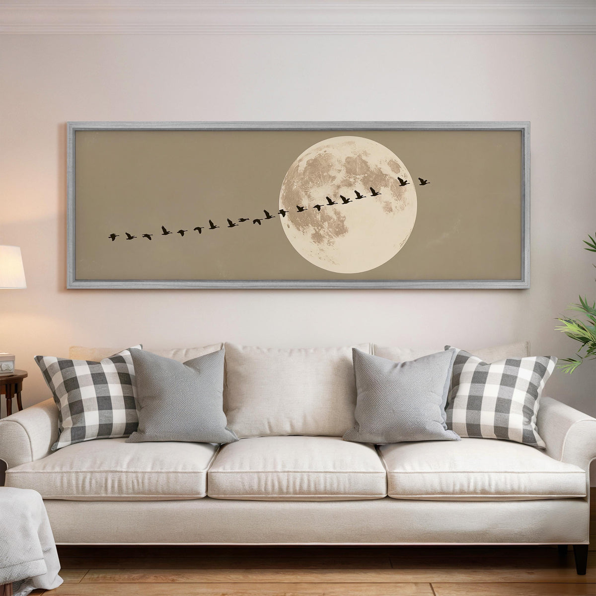 Geese flying past a full moon panoramic canvas print above a white sofa in a bright living room