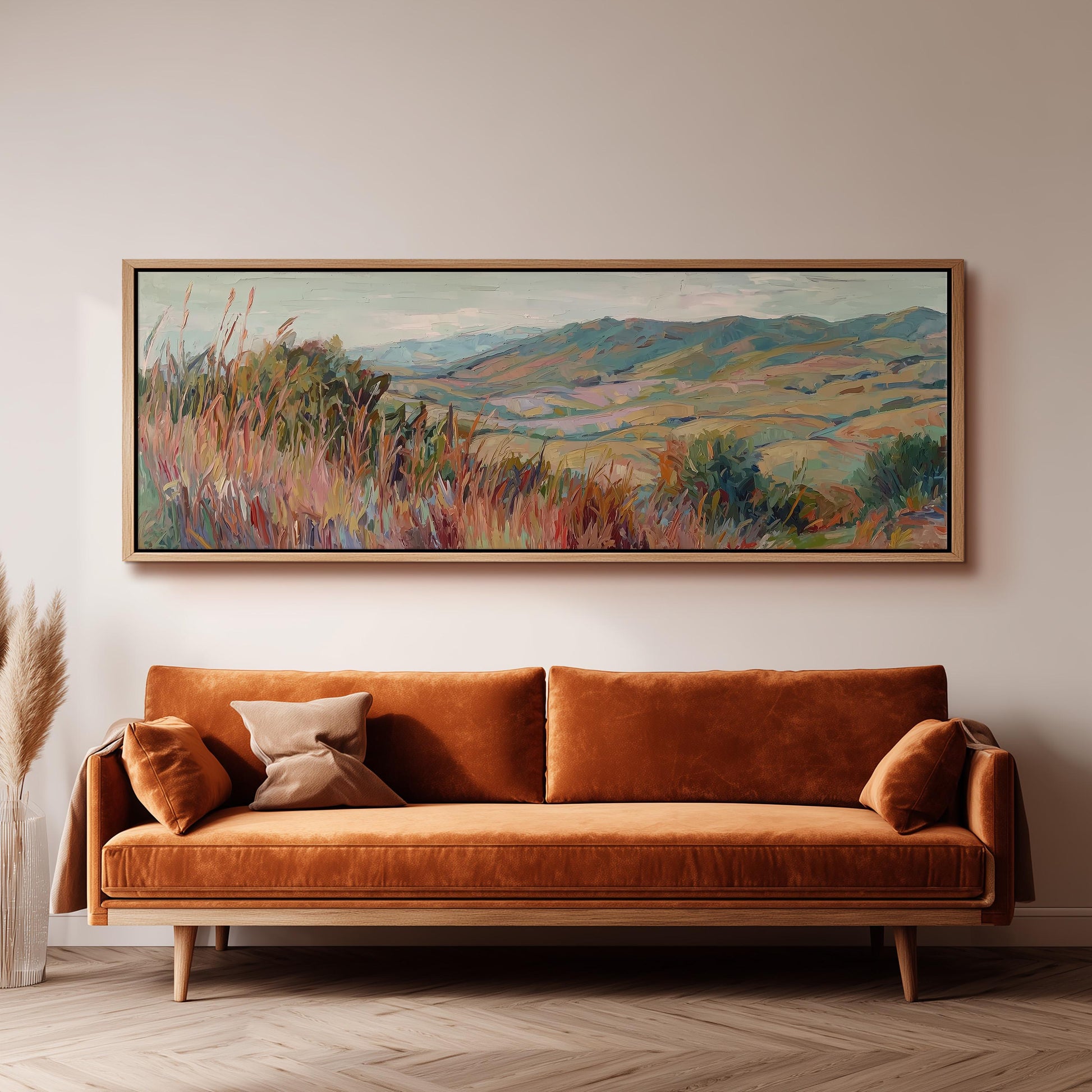 a large, colorful landscape painting hanging on a wall above a brown sofa with orange cushions.