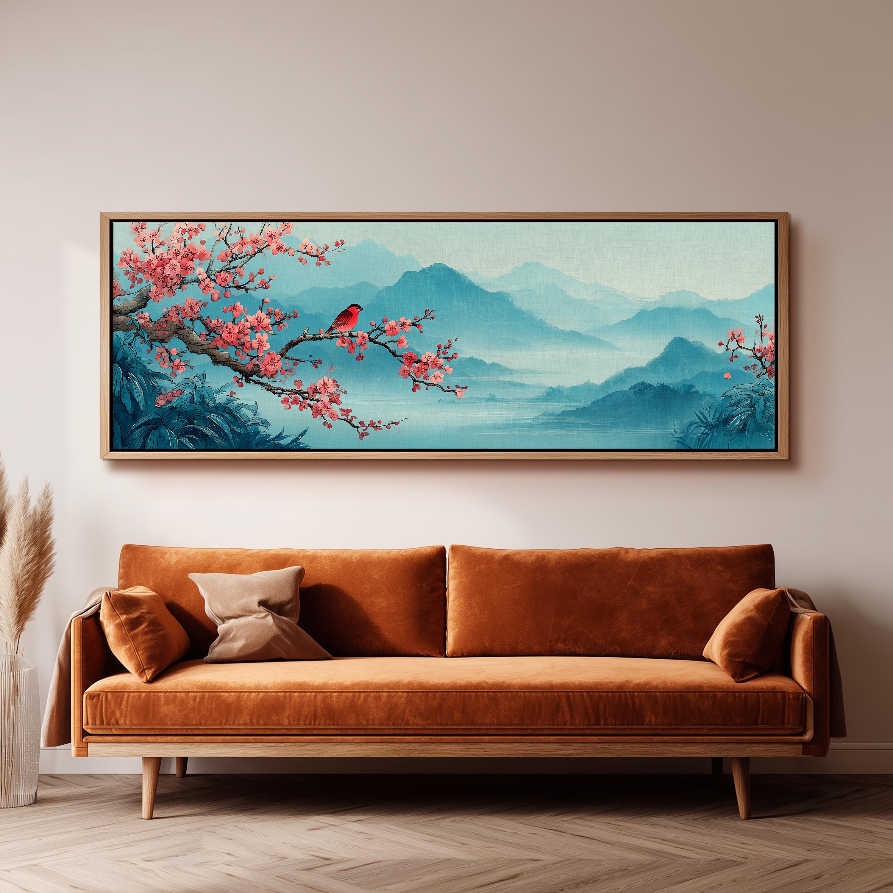 a large, framed painting of a serene landscape with a bird perched on a branch, surrounded by pink flowers and mountains in the background. The painting is hung on a wall above a brown sofa, creating a cozy and inviting atmosphere in the room.