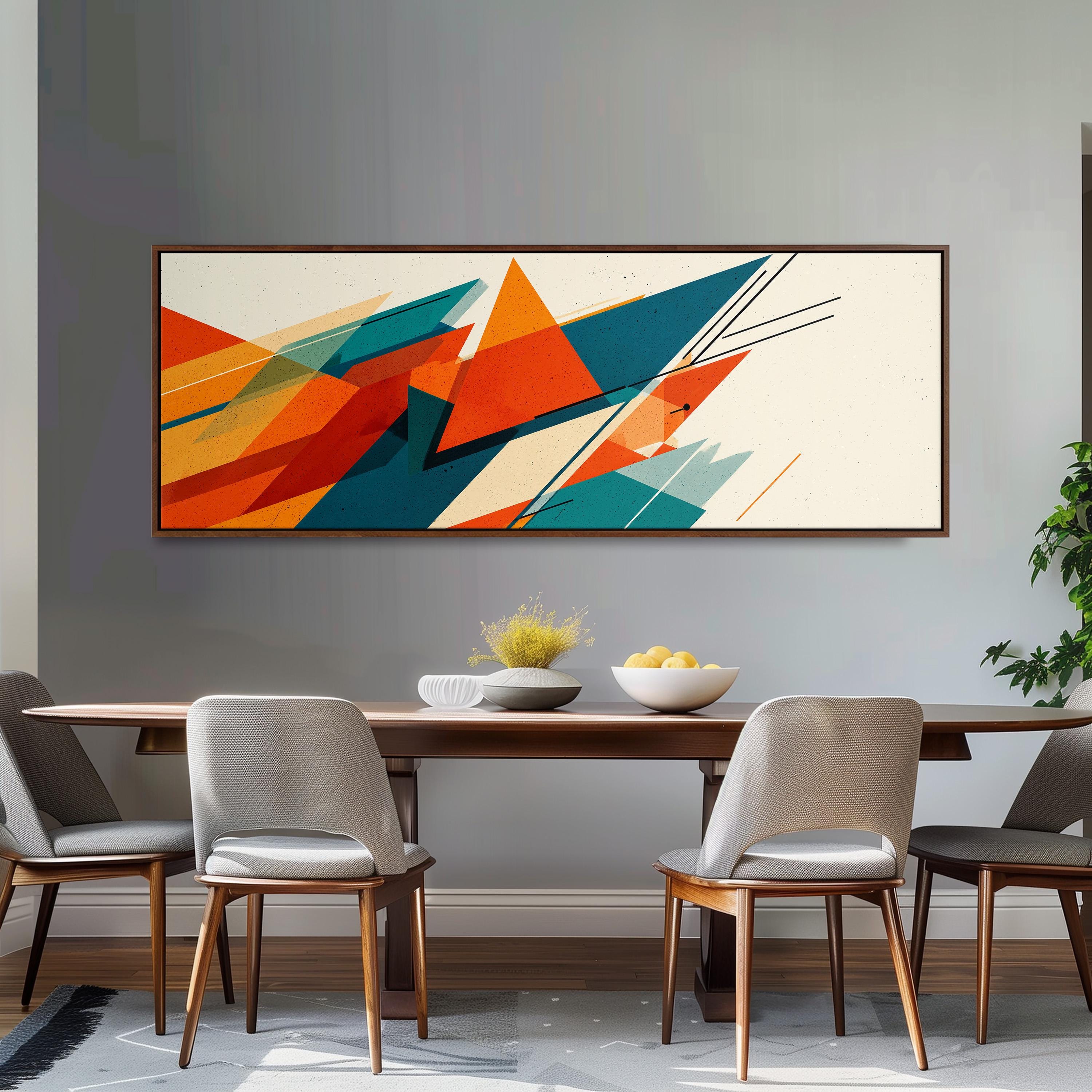 a modern dining room with a wooden table and four gray chairs. Above the table, there is a large abstract painting with vibrant orange, green, and blue geometric shapes. The painting is framed and hangs on the wall above the dining area.