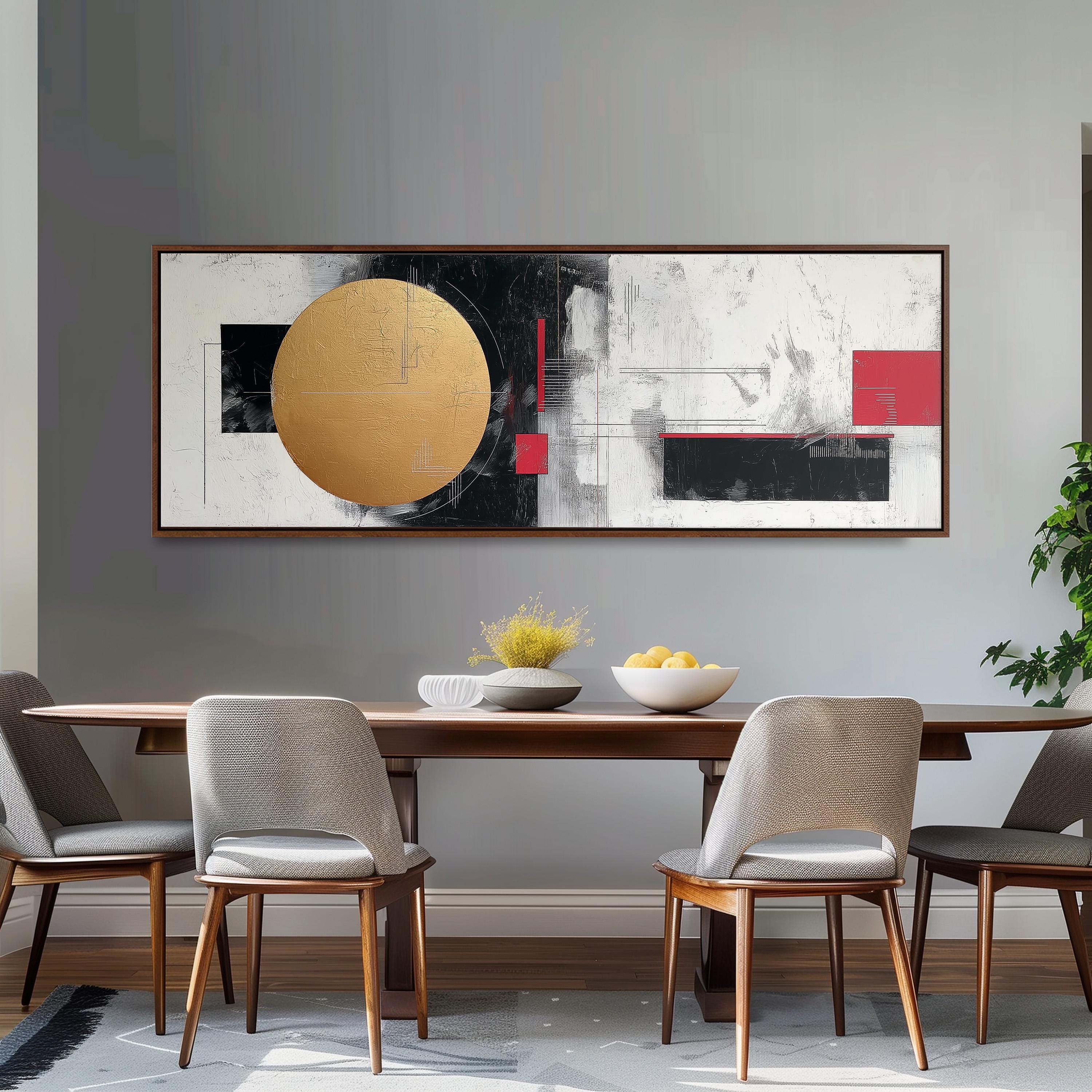 a modern dining room with a wooden table and four upholstered chairs. Above the table, there is a large abstract painting with bold black, white, and red colors. The painting is framed and hangs on the wall above the table. On the table, there is a bowl of fruit and a vase of flowers, adding a touch of elegance to the setting.