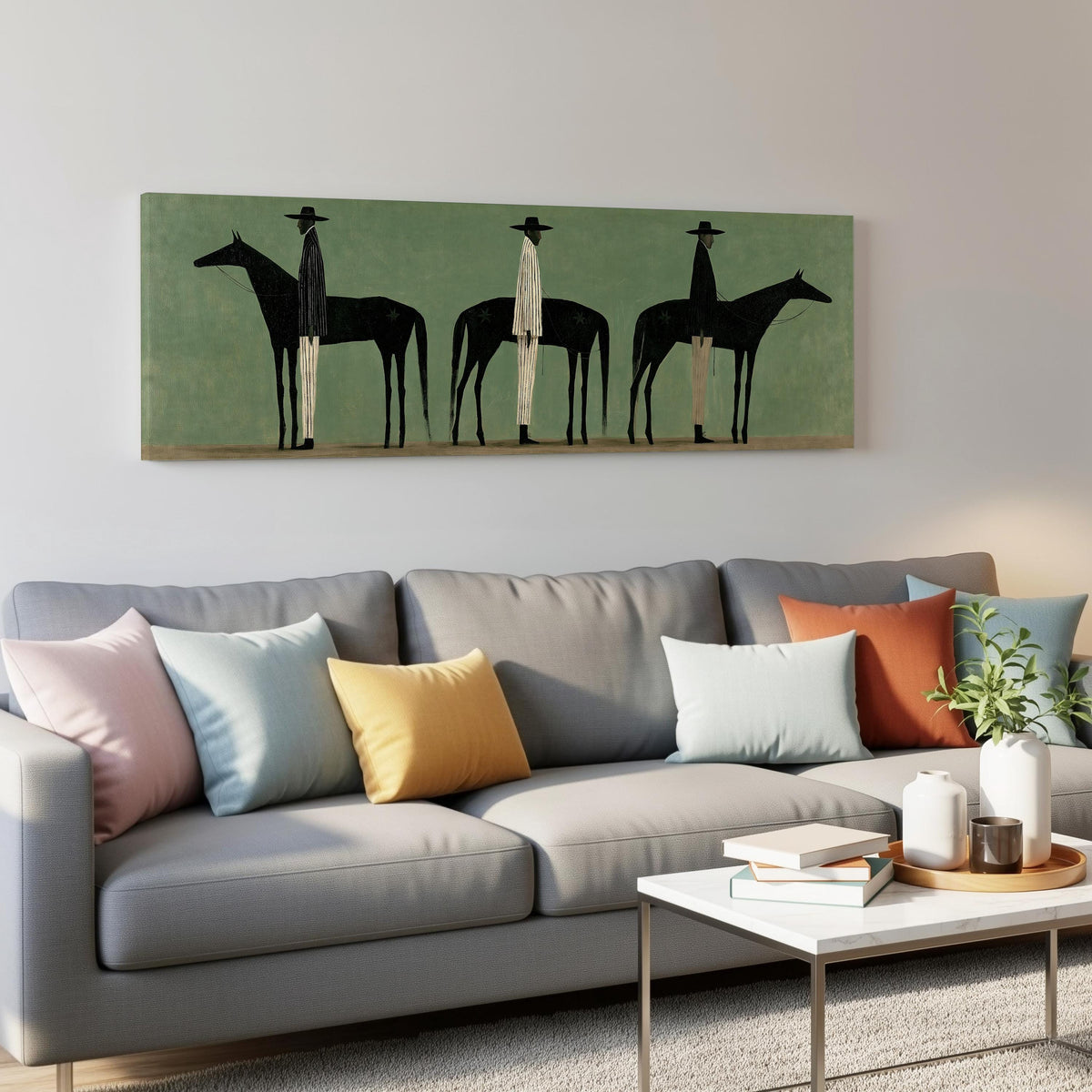 Three stylized cowboys with horses on sage green panoramic canvas print above a grey sofa in a living room
