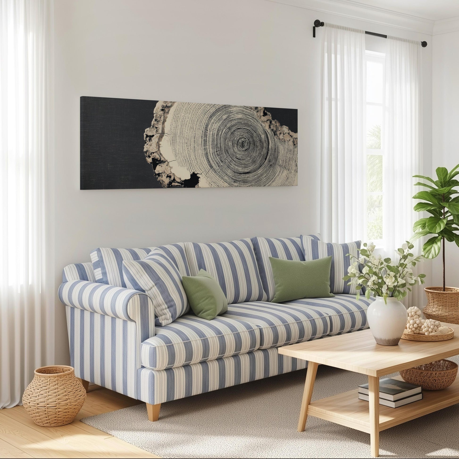 a cozy living room with a striped blue and white sofa, a wooden coffee table, and a large window with white curtains. A large black and white tree trunk artwork is displayed on the wall above the sofa, and a potted plant is placed on the coffee table.