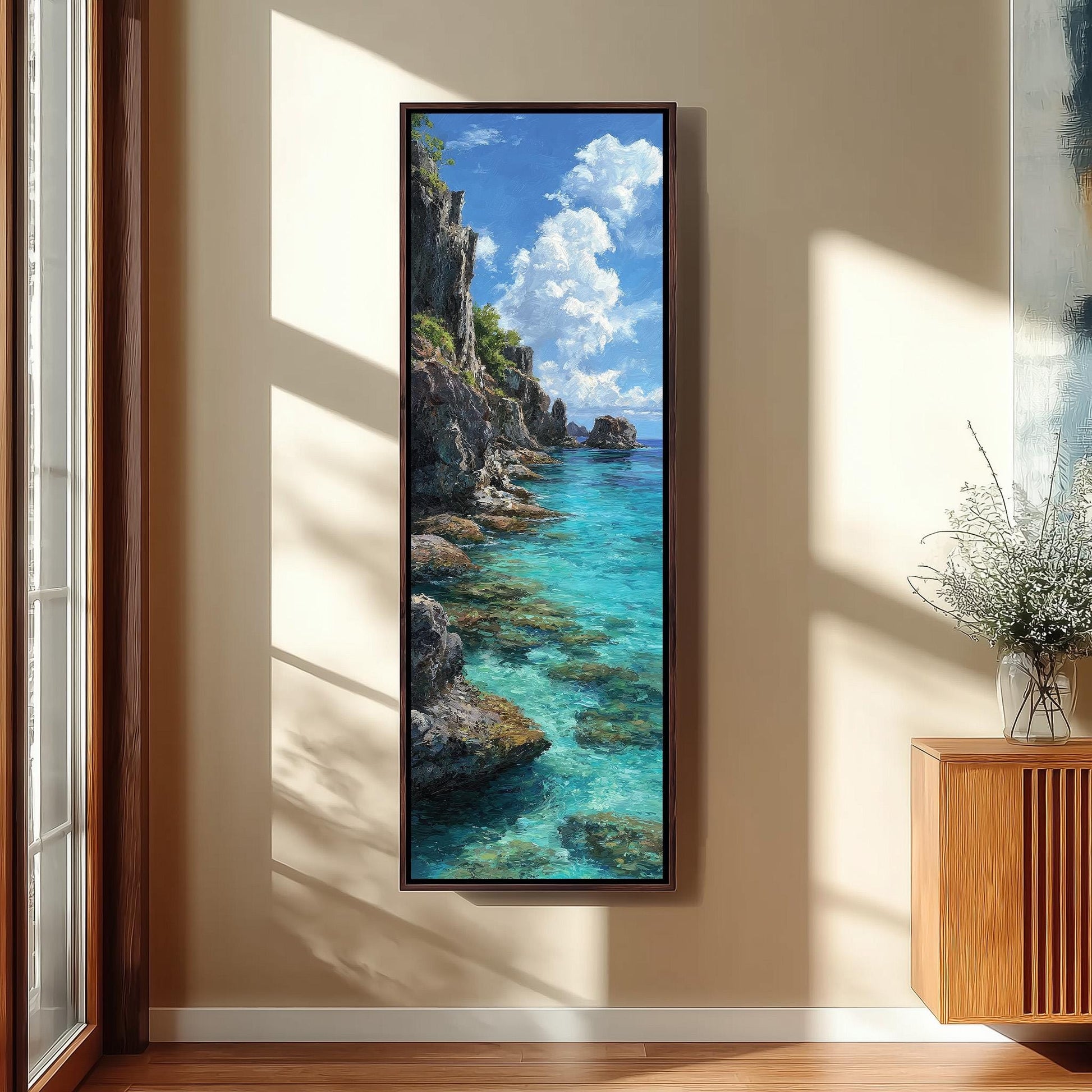a large framed painting of a serene coastal landscape, with a rocky cliff overlooking a turquoise sea. The painting is hung on a wall in a room with a wooden floor and a window, creating a peaceful and natural atmosphere.