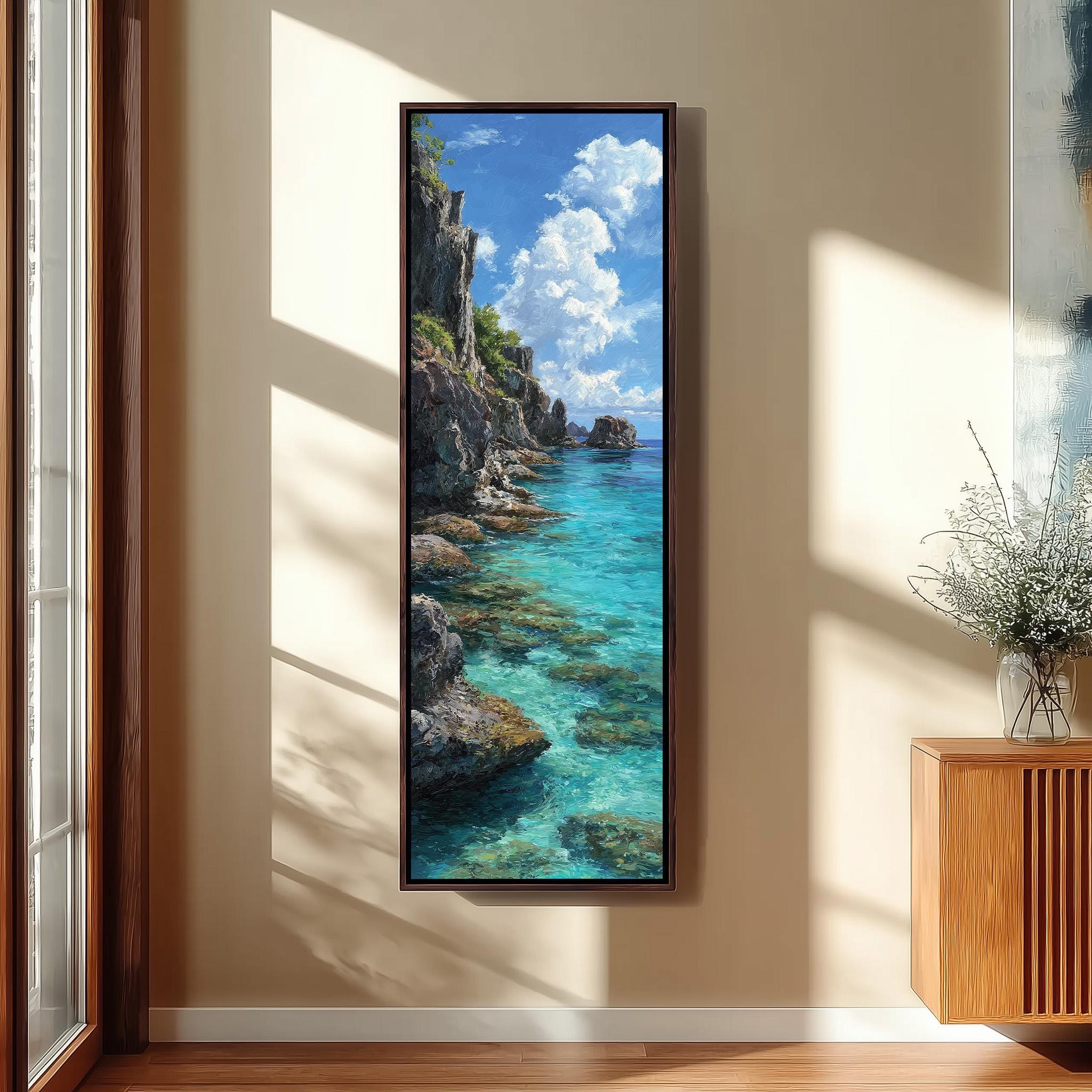 a large framed painting of a serene coastal landscape, with a rocky cliff overlooking a turquoise sea. The painting is hung on a wall in a room with a wooden floor and a window, creating a peaceful and natural atmosphere.