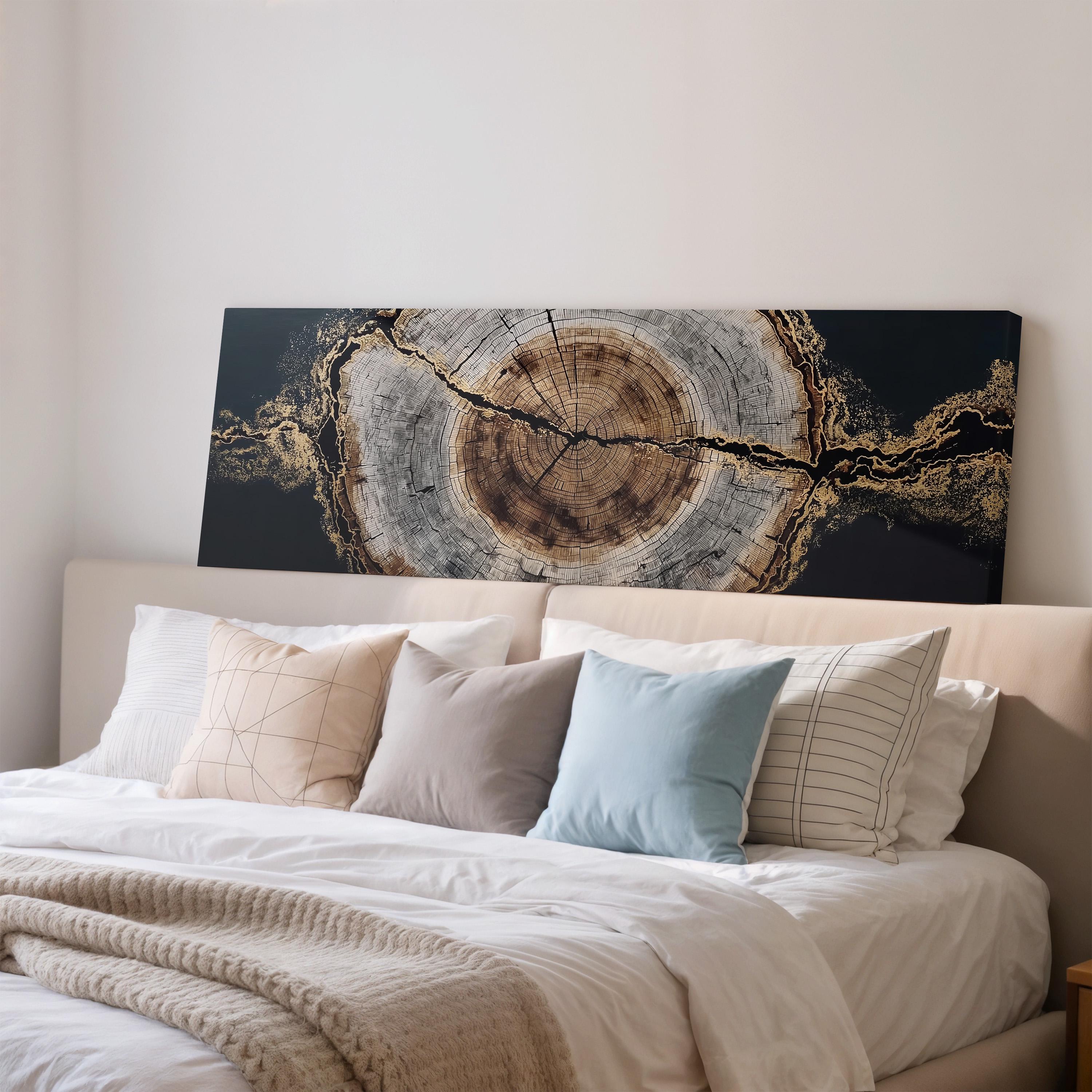 a large bed with a white comforter and a variety of pillows, including a blue pillow and a striped pillow. Above the bed, there is a large black and gold artwork depicting a tree trunk with a cross-section view.