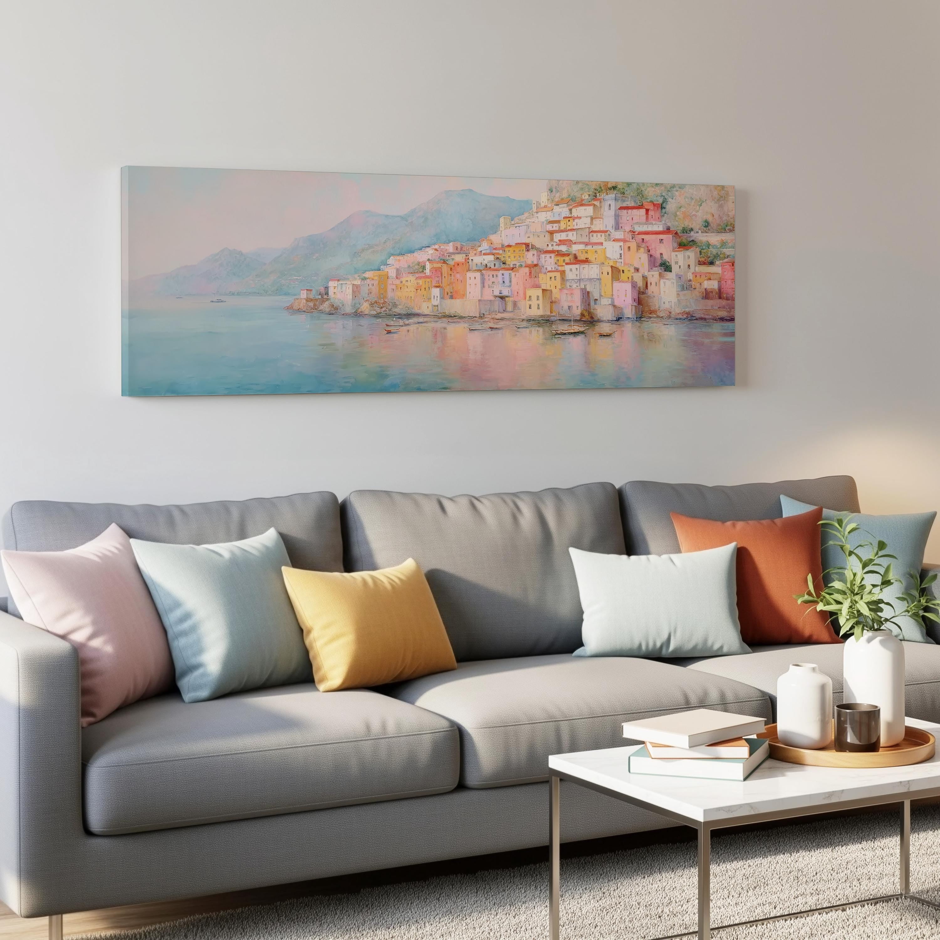a living room with a gray sofa adorned with colorful throw pillows, a white coffee table, and a large painting of a coastal town hanging on the wall above the sofa.