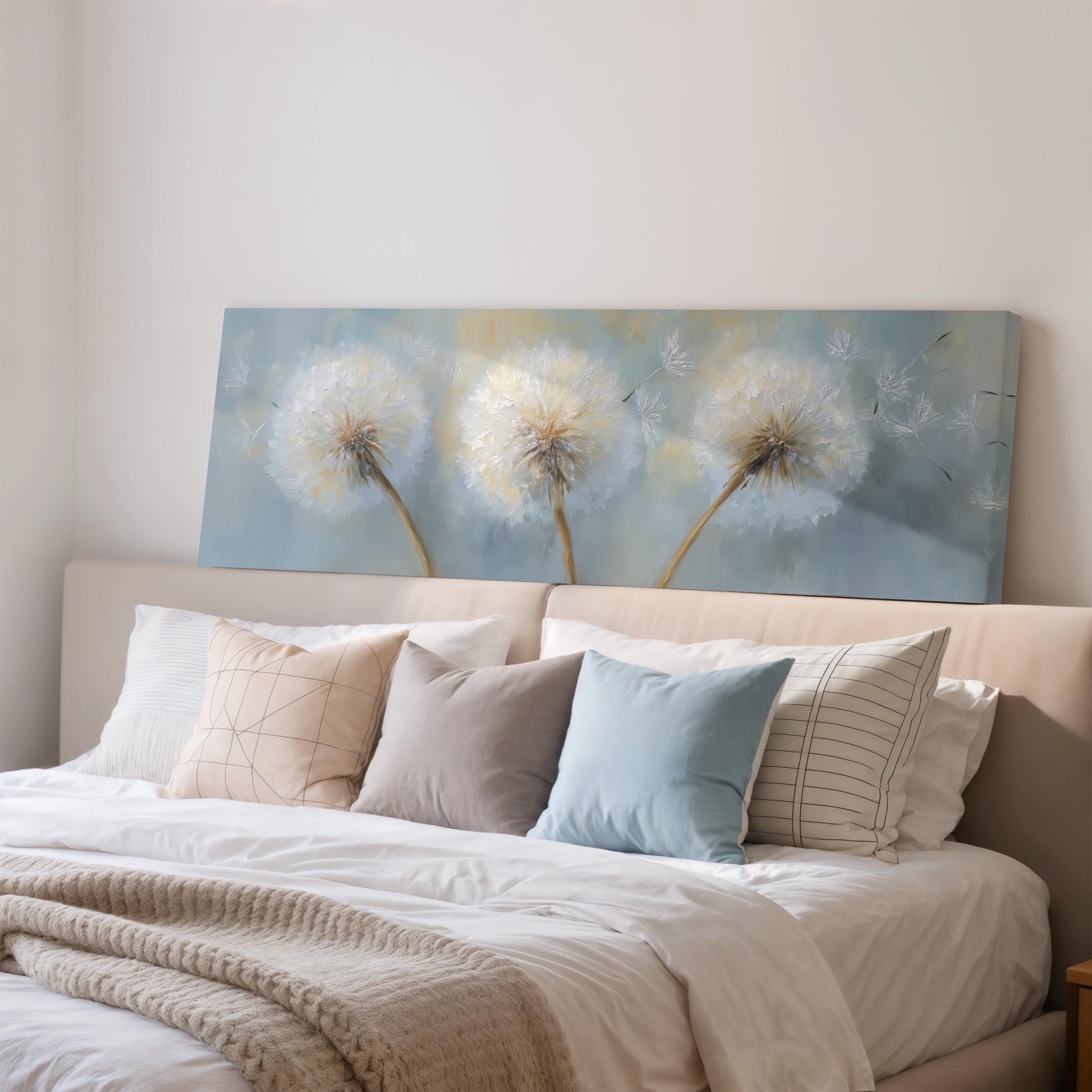a bedroom with a large bed adorned with white pillows and a blue blanket. Above the bed, there is a painting of three dandelions against a blue background.