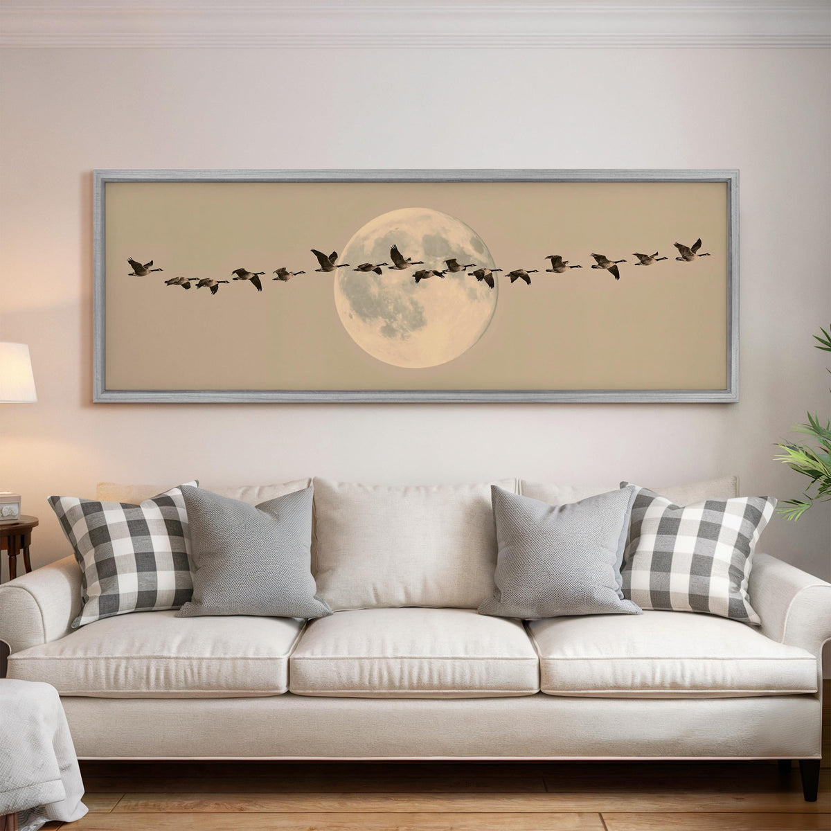 Geese flying across a pale moon on sand panoramic canvas print above a white sofa in a bright living room