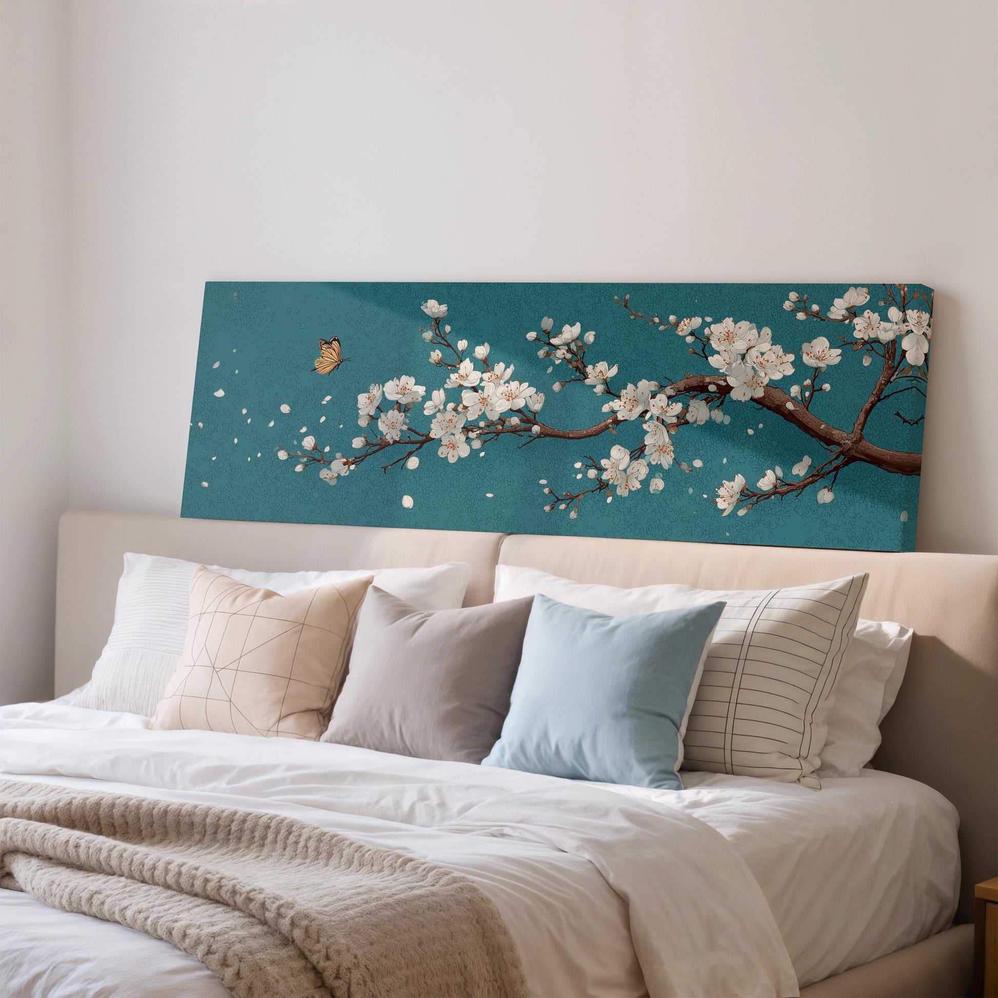 a bedroom with a large bed adorned with white pillows and a blue blanket. Above the bed, there is a large canvas print depicting a branch of white flowers against a teal background.