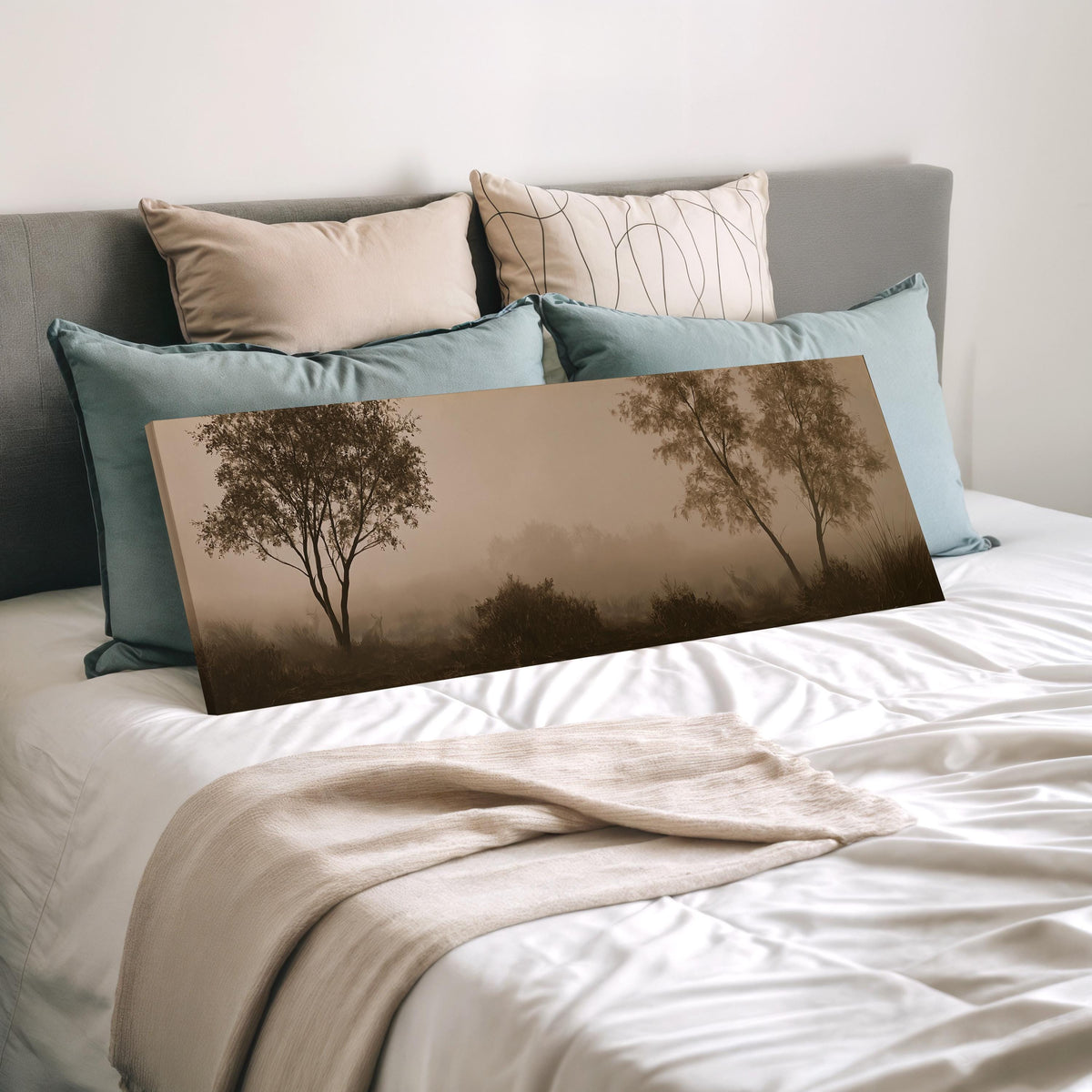 Two trees in sepia fog wide panoramic canvas print laid on a bed to show its size