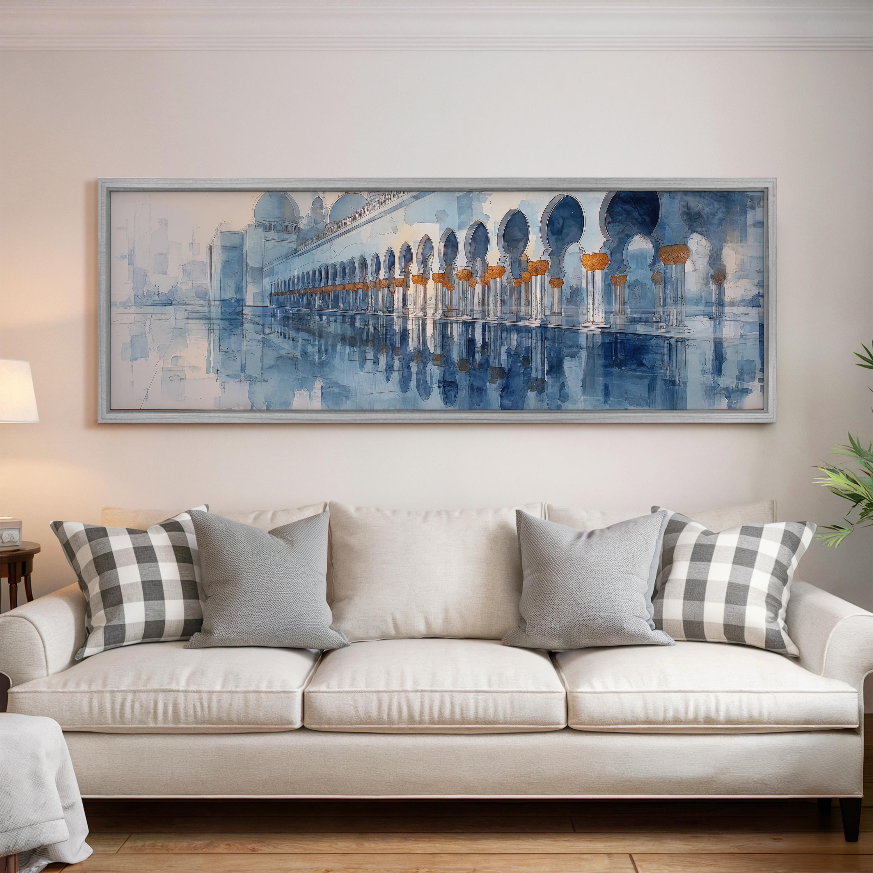 a large, framed painting of a building with arches hanging on a wall above a white sofa with gray and white pillows.