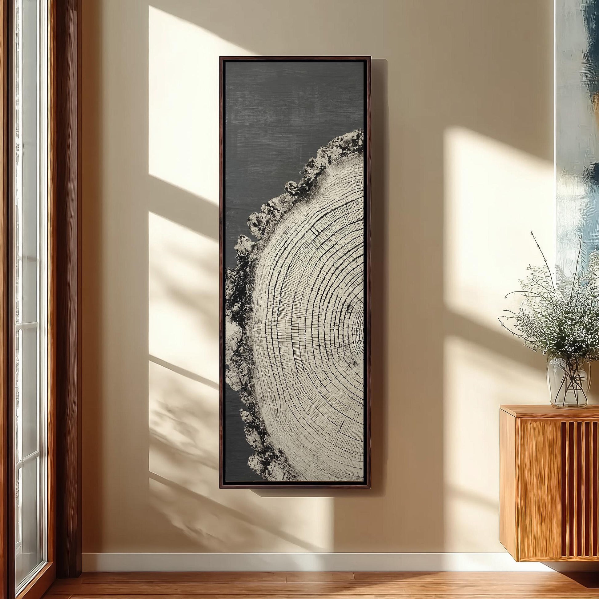 a large, framed artwork depicting a tree stump with concentric rings, hanging on a wall in a room with a wooden cabinet and a vase of flowers.