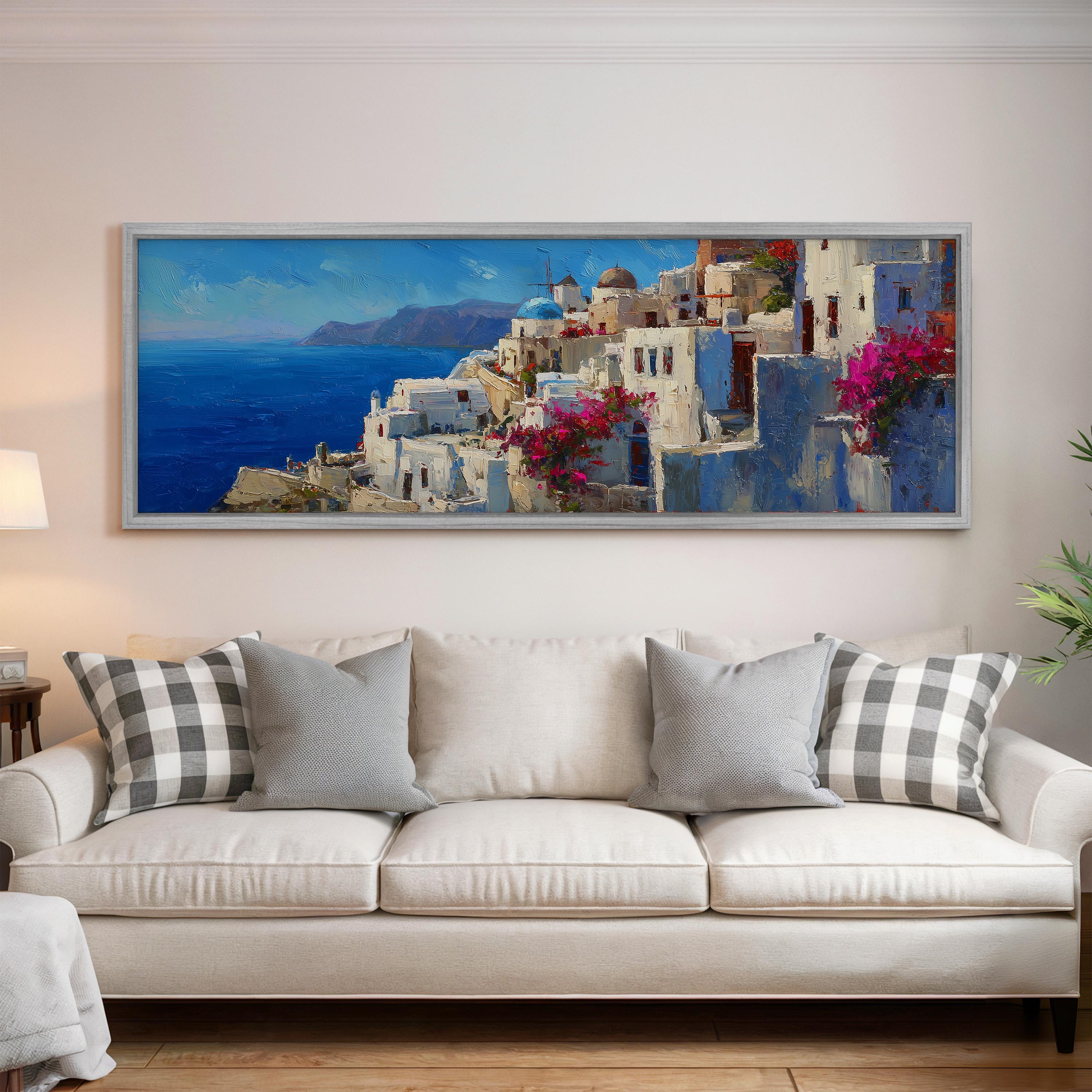 a large, framed painting of a picturesque coastal town with white buildings, blue roofs, and pink flowers, hanging on a wall above a white couch with gray and white patterned pillows.
