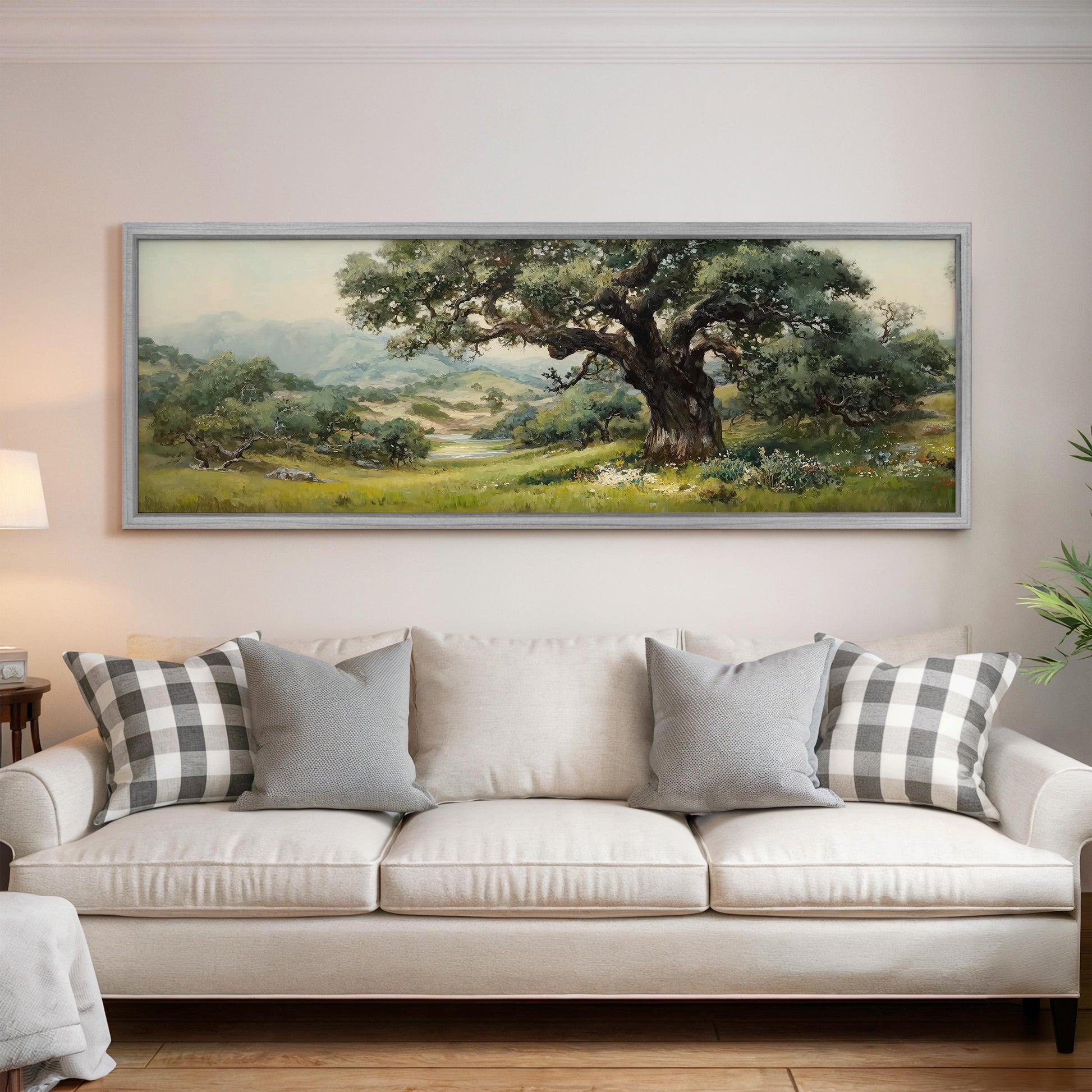 a large painting of a tree and a landscape hanging on a wall above a white sofa with gray and white plaid throw pillows.