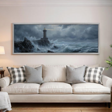 a large painting of a lighthouse on a stormy sea hanging on a wall above a white sofa with patterned throw pillows.