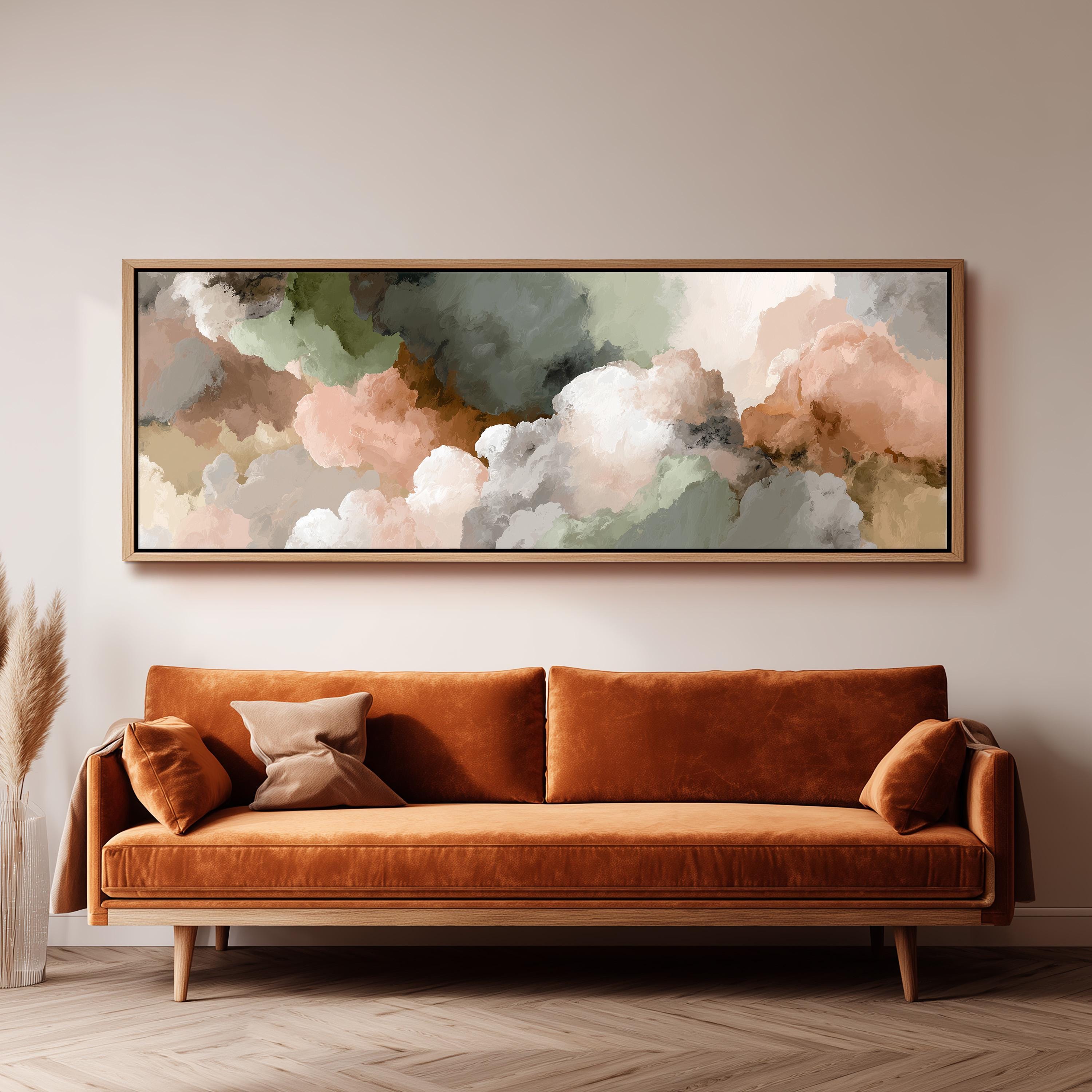 a large, framed painting of clouds hanging on a wall above a brown sofa with orange cushions.