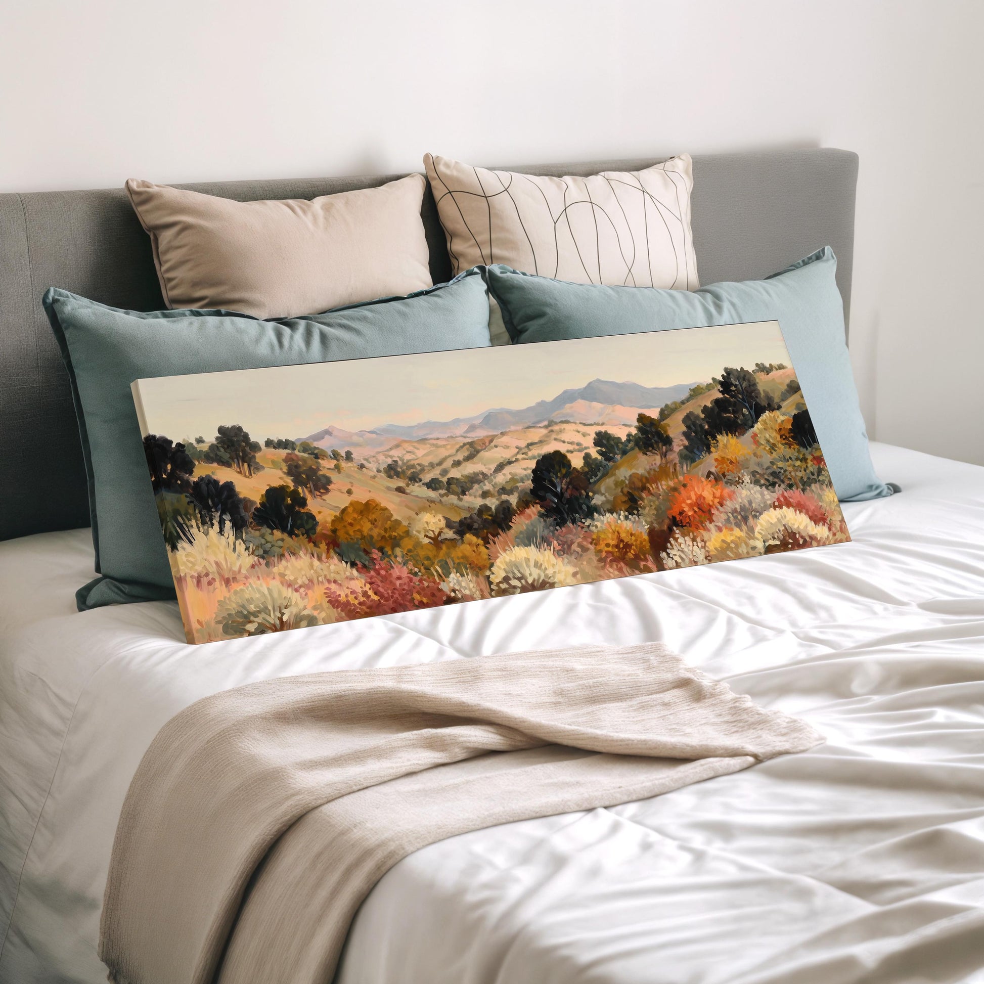 a large landscape painting displayed on a bed, surrounded by pillows.