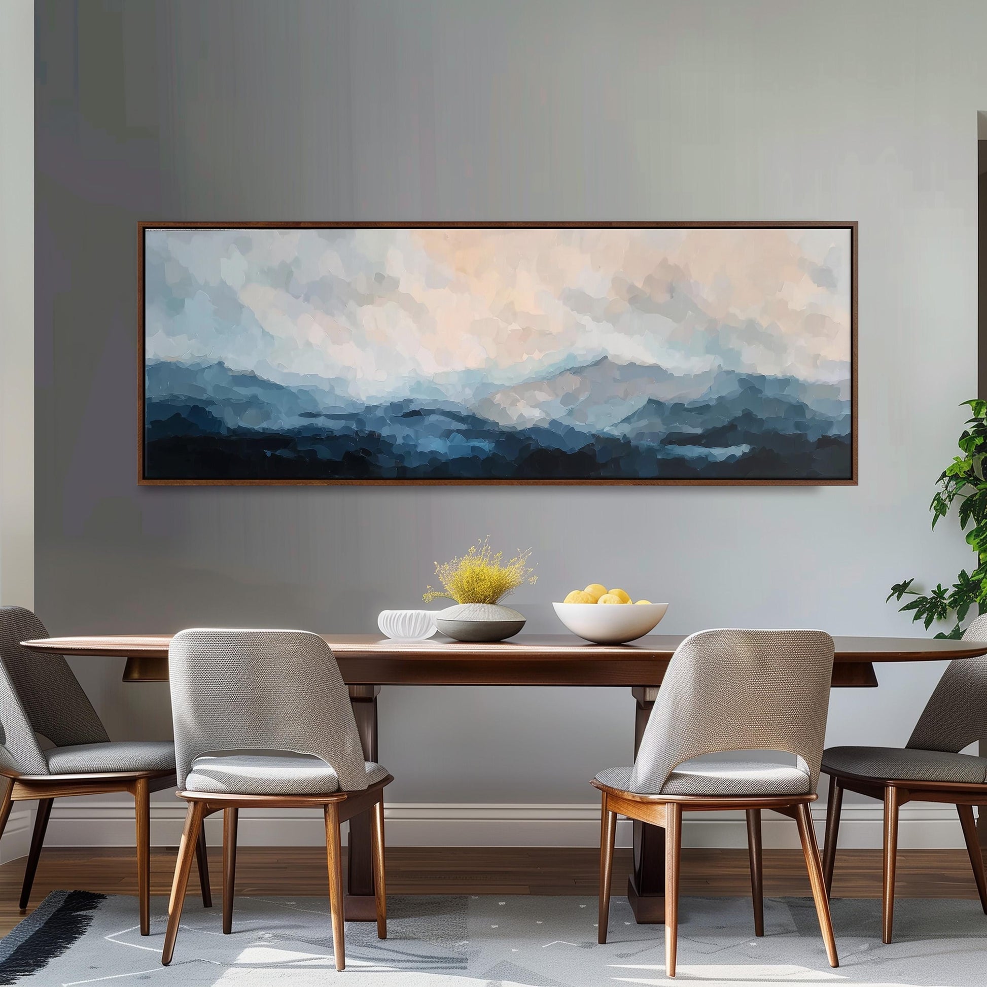 a dining room with a large painting of a mountain landscape hanging on the wall above a wooden dining table with four chairs. The table is set with a bowl of fruit and a vase of flowers, creating a cozy and inviting atmosphere.