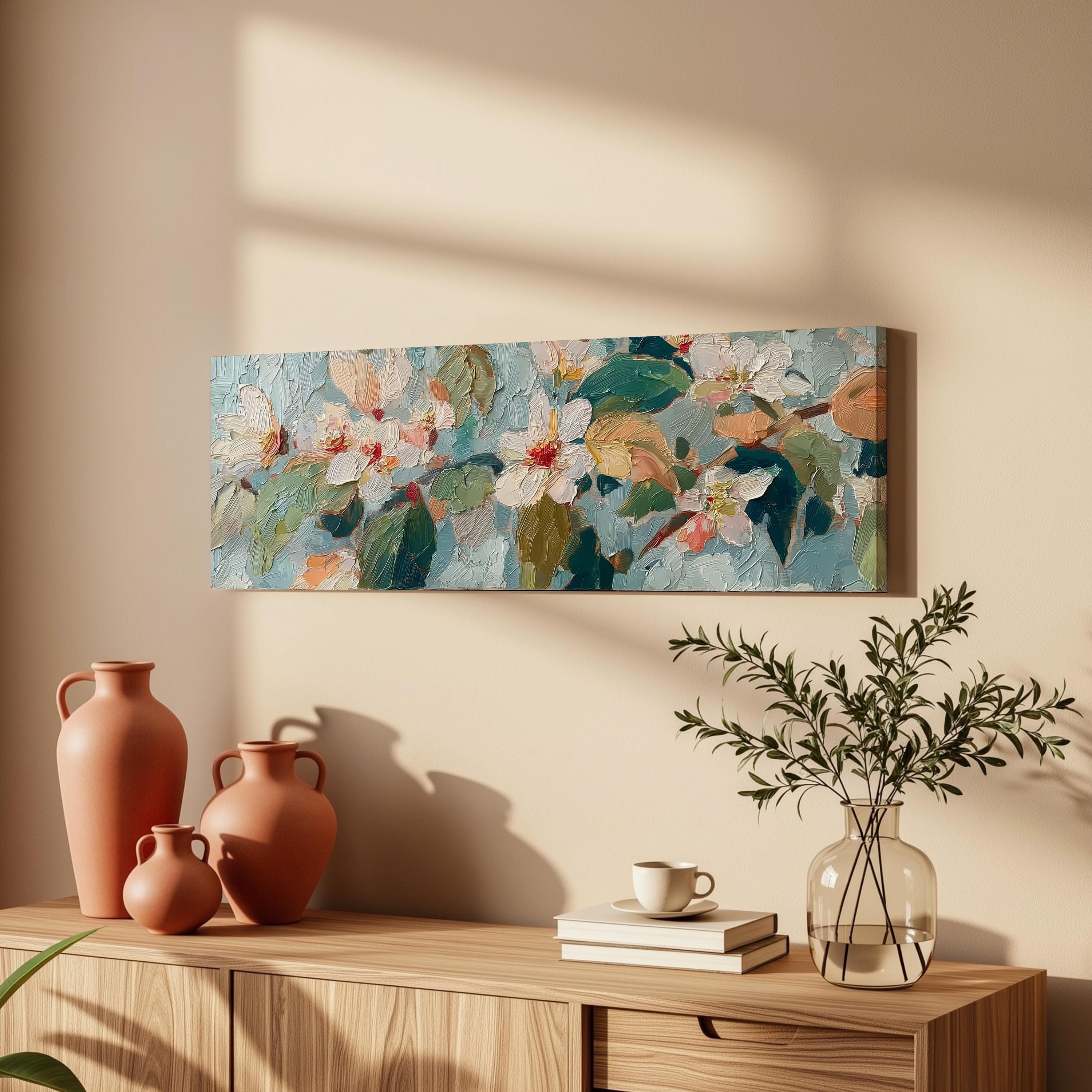 a wooden cabinet with a vase, a stack of books, and a coffee cup on top. Above the cabinet, there is a painting of flowers hanging on the wall.