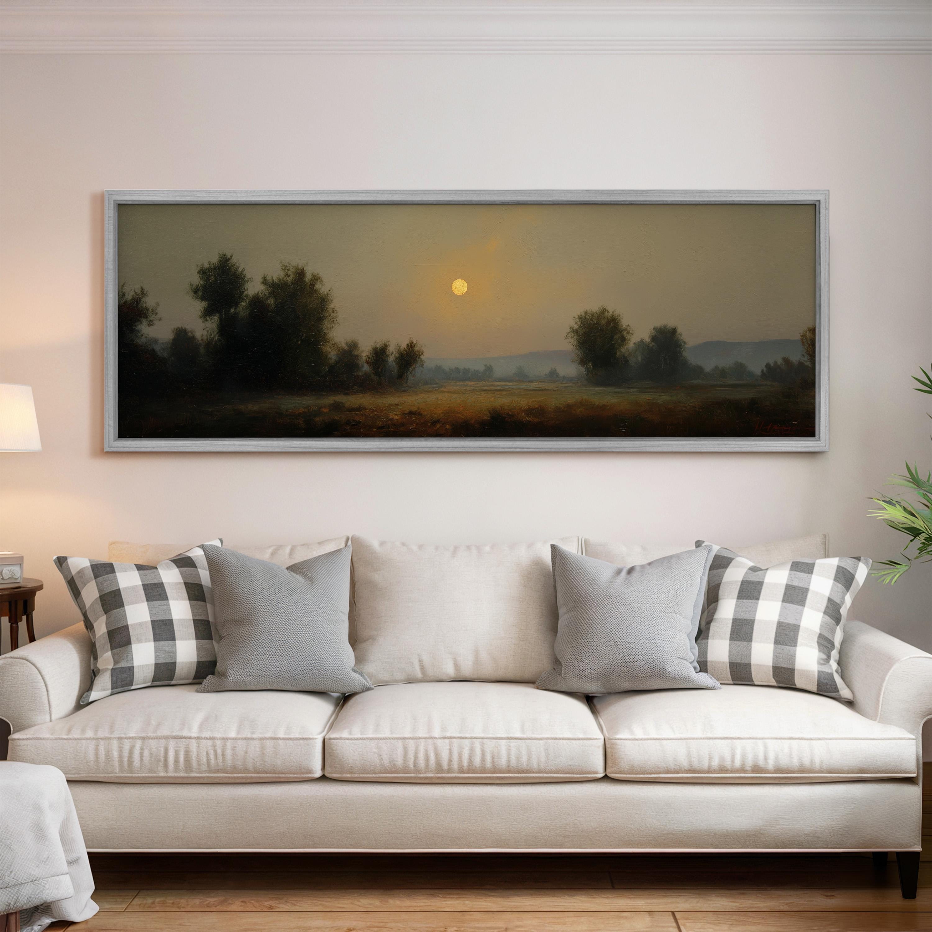 a large painting of a landscape with a sunset over a field, hanging on a wall above a white sofa with patterned throw pillows.