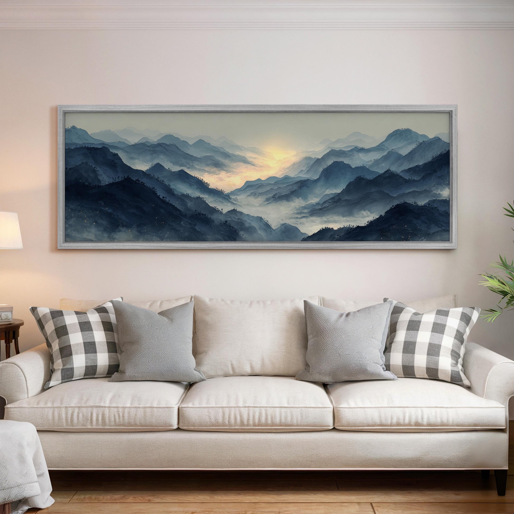 a large, framed painting of a mountainous landscape hanging on a wall above a white sofa with gray and white patterned pillows.