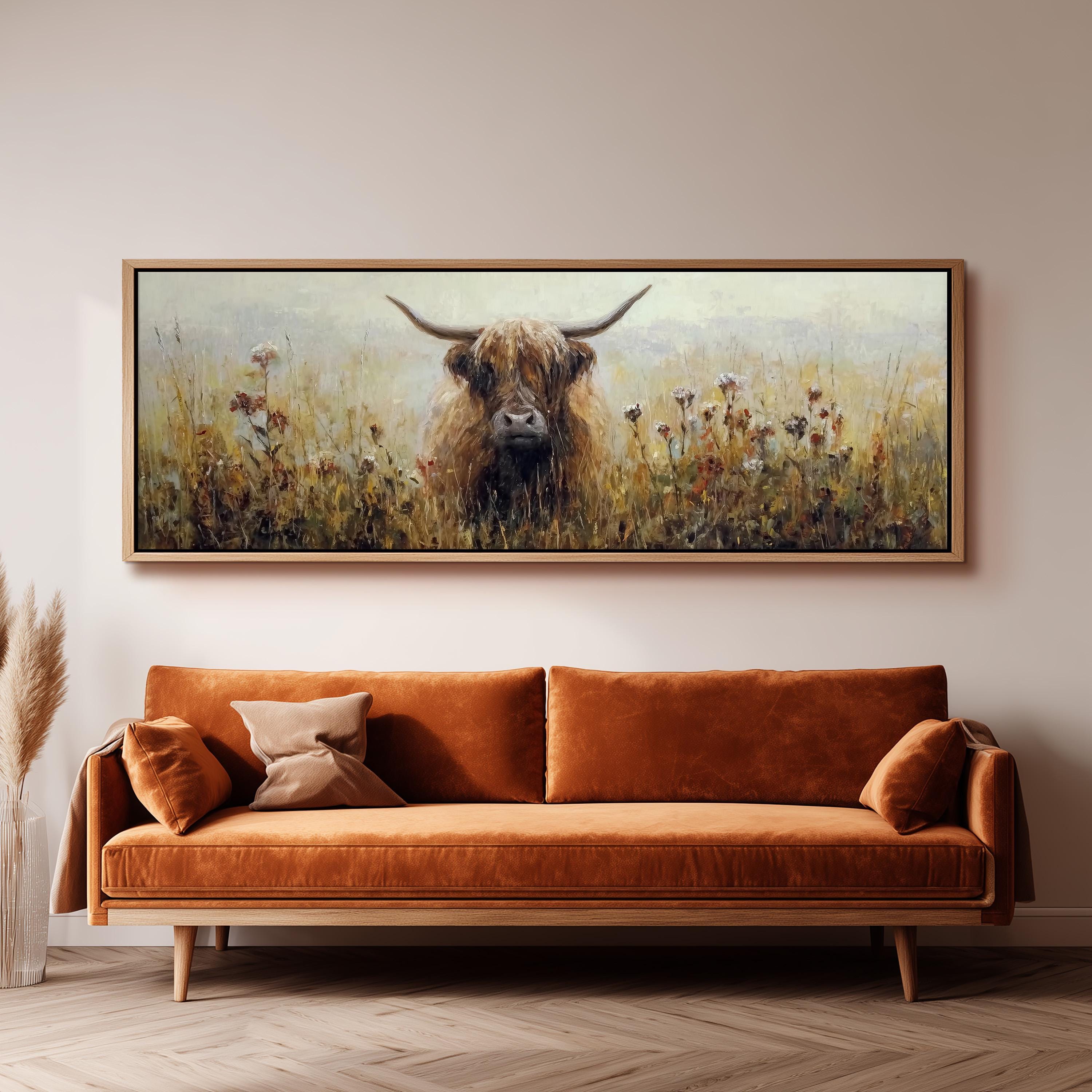 a large painting of a Highland cow in a field, hanging on a wall above a brown sofa.