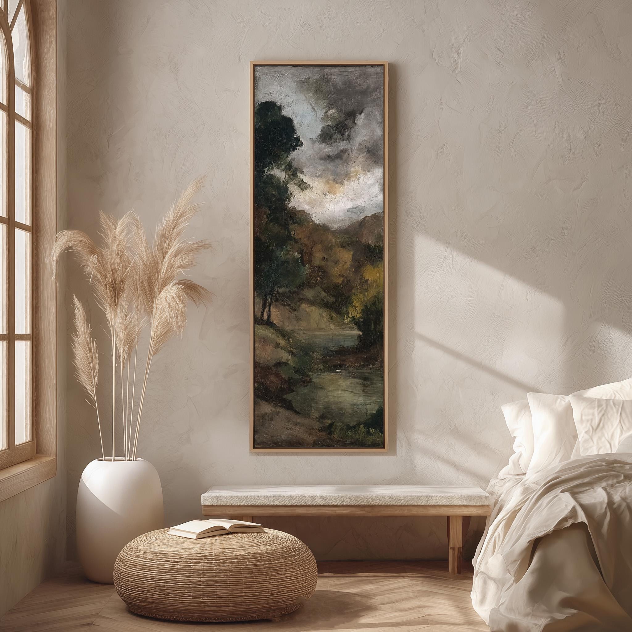 a serene and cozy bedroom scene, featuring a large painting of a landscape hanging on the wall, a white bed with a white pillow, a white vase with tall potted plants, and a woven ottoman with a book on it.