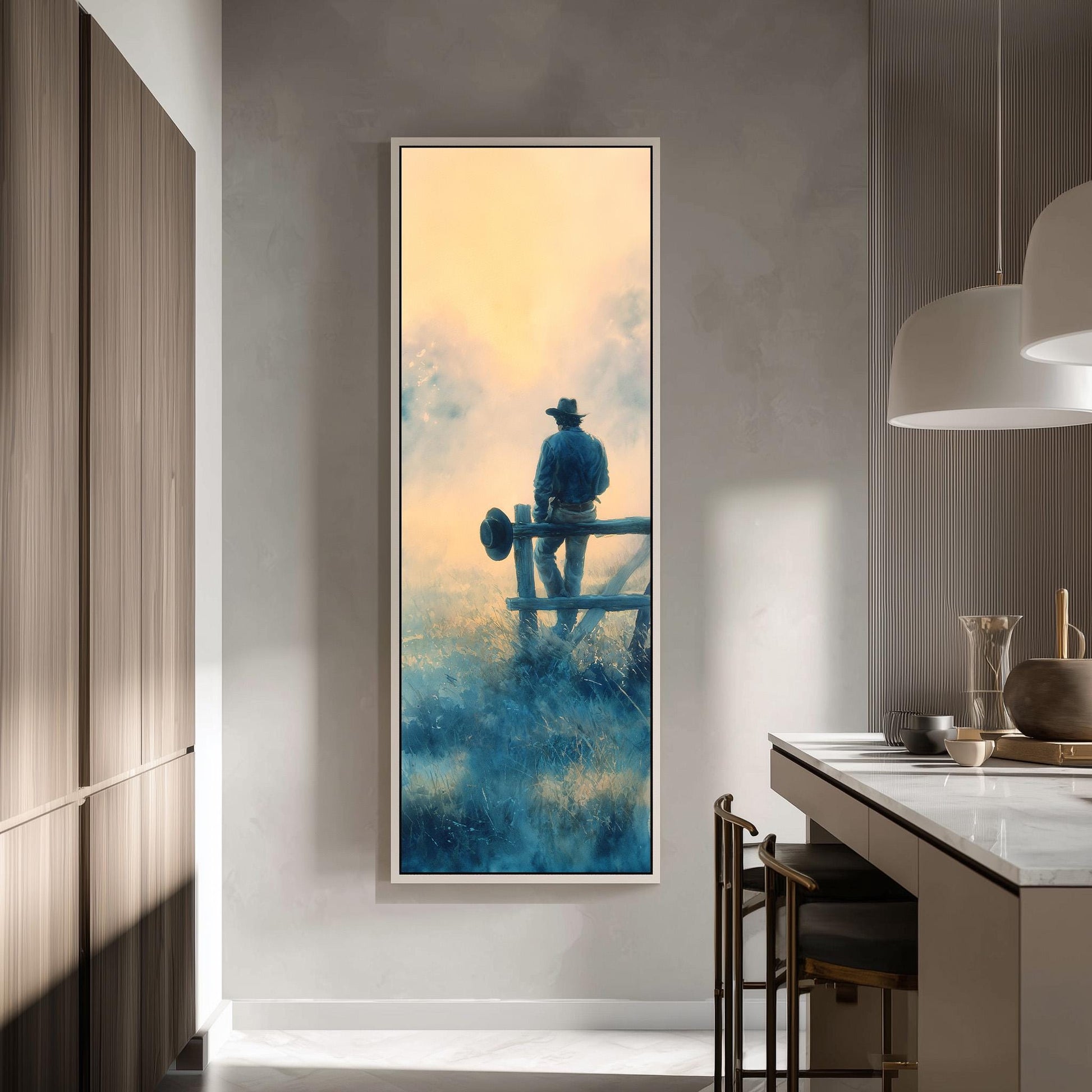 a large painting of a cowboy sitting on a fence, with a serene landscape in the background. The painting is hanging on a wall in a modern kitchen, with a countertop and chairs visible in the foreground.